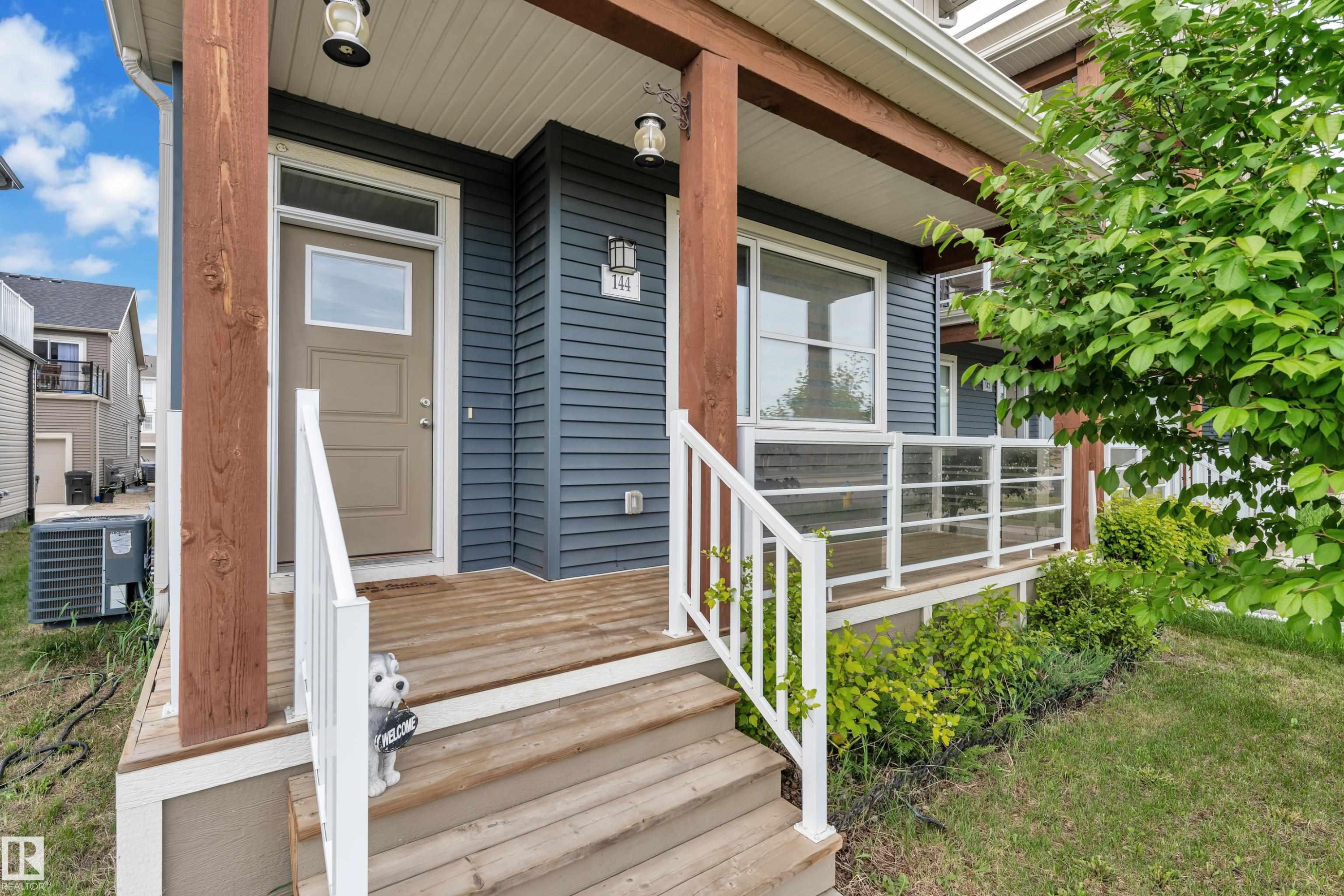 Covered porch featuring wood-finish decking and steps, dark blue horizontal siding, and robust wood support beams - 144 Sunwapta Way, Edmonton, AB
