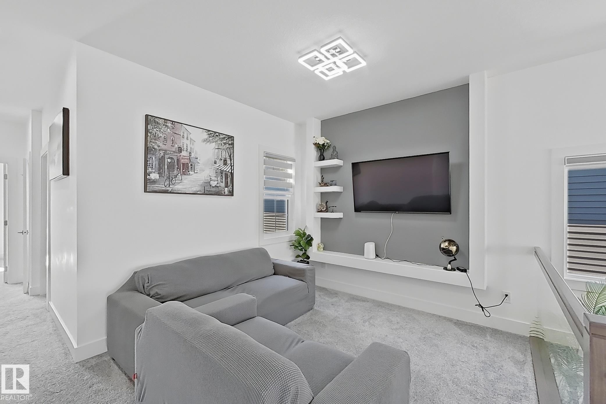Carpeted landing area featuring a modern flush-mount ceiling light fixture, a media wall with a contrasting accent panel, built-in shelving, and a built-in media console - 415 42 Street, Edmonton, AB