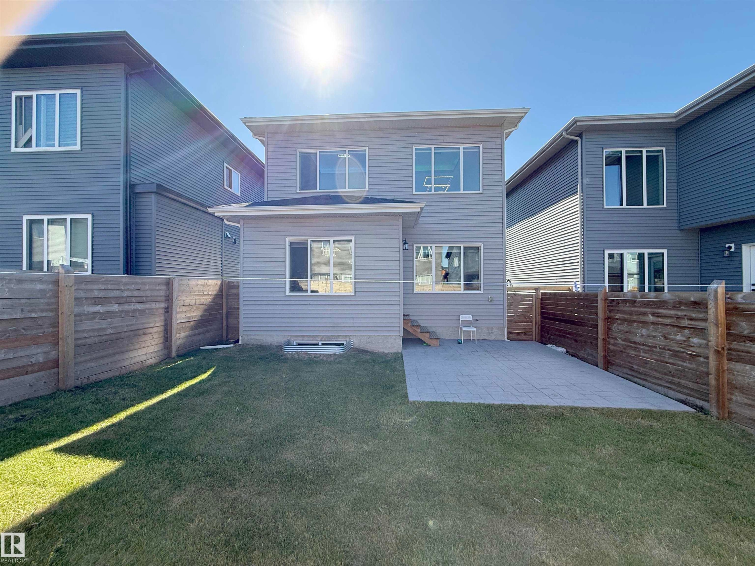 Exterior featuring light gray siding with white trim, multiple windows, a rear patio with paver stones, a grass lawn, and wood privacy fencing - 415 42 Street, Edmonton, AB