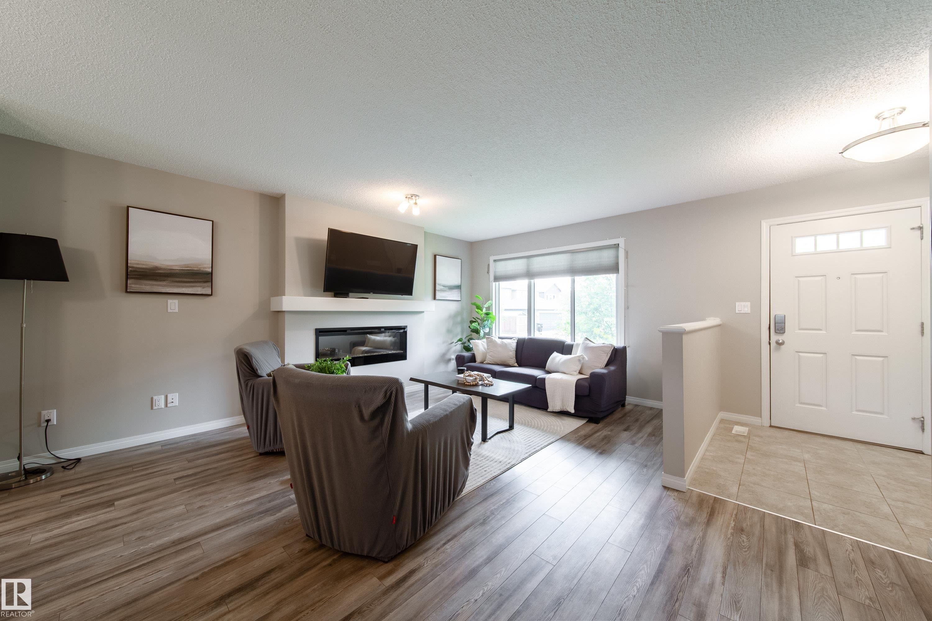 Spacious living area featuring wood-finish flooring, a contemporary fireplace with a white mantel, and ample natural light from large windows - 3211 Cherry Crescent, Edmonton, AB