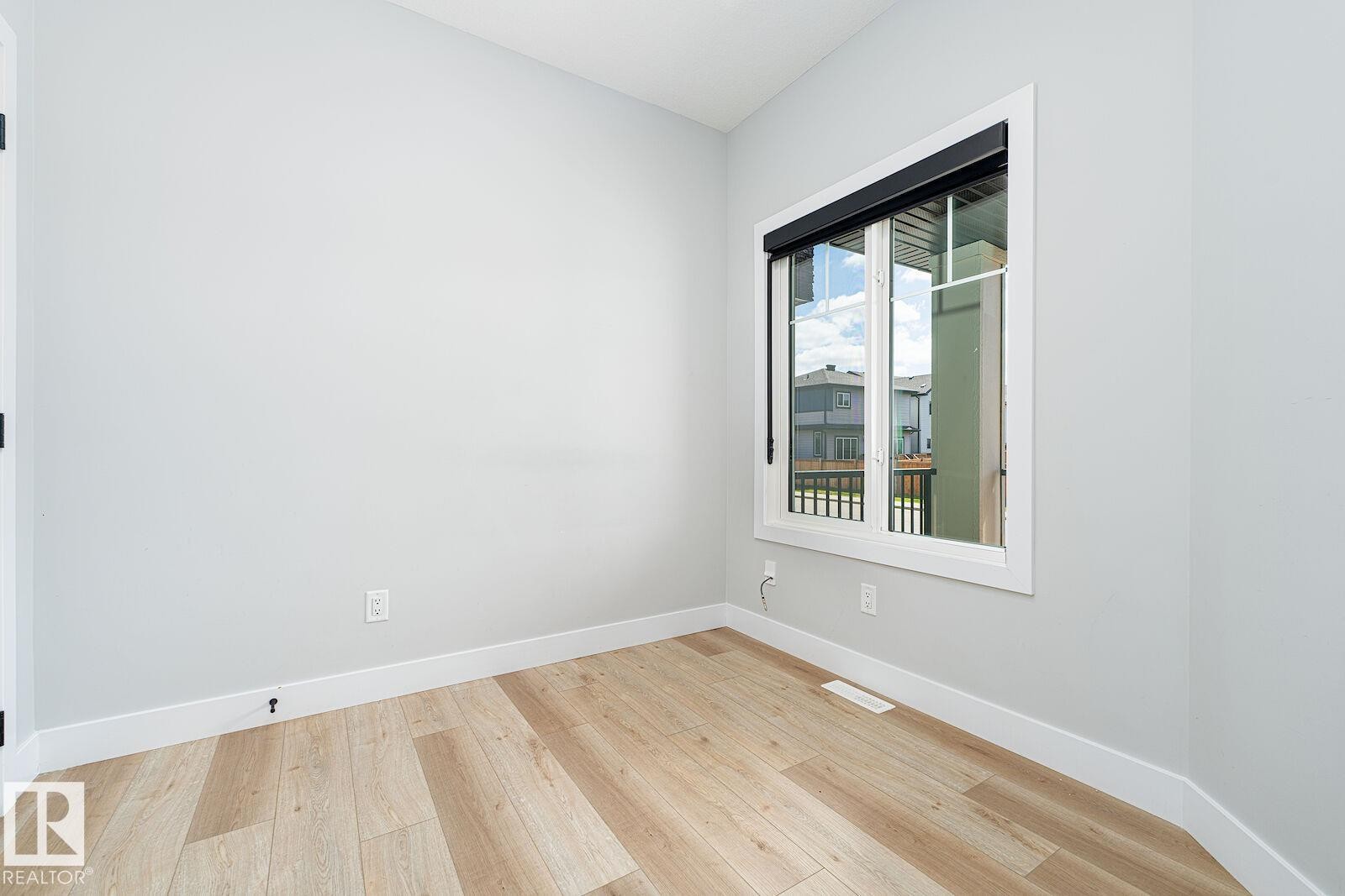 Bright room featuring a prominent window, light wood-finish flooring, white baseboards, and neutral wall paint - 17320 9 Avenue, Edmonton, AB