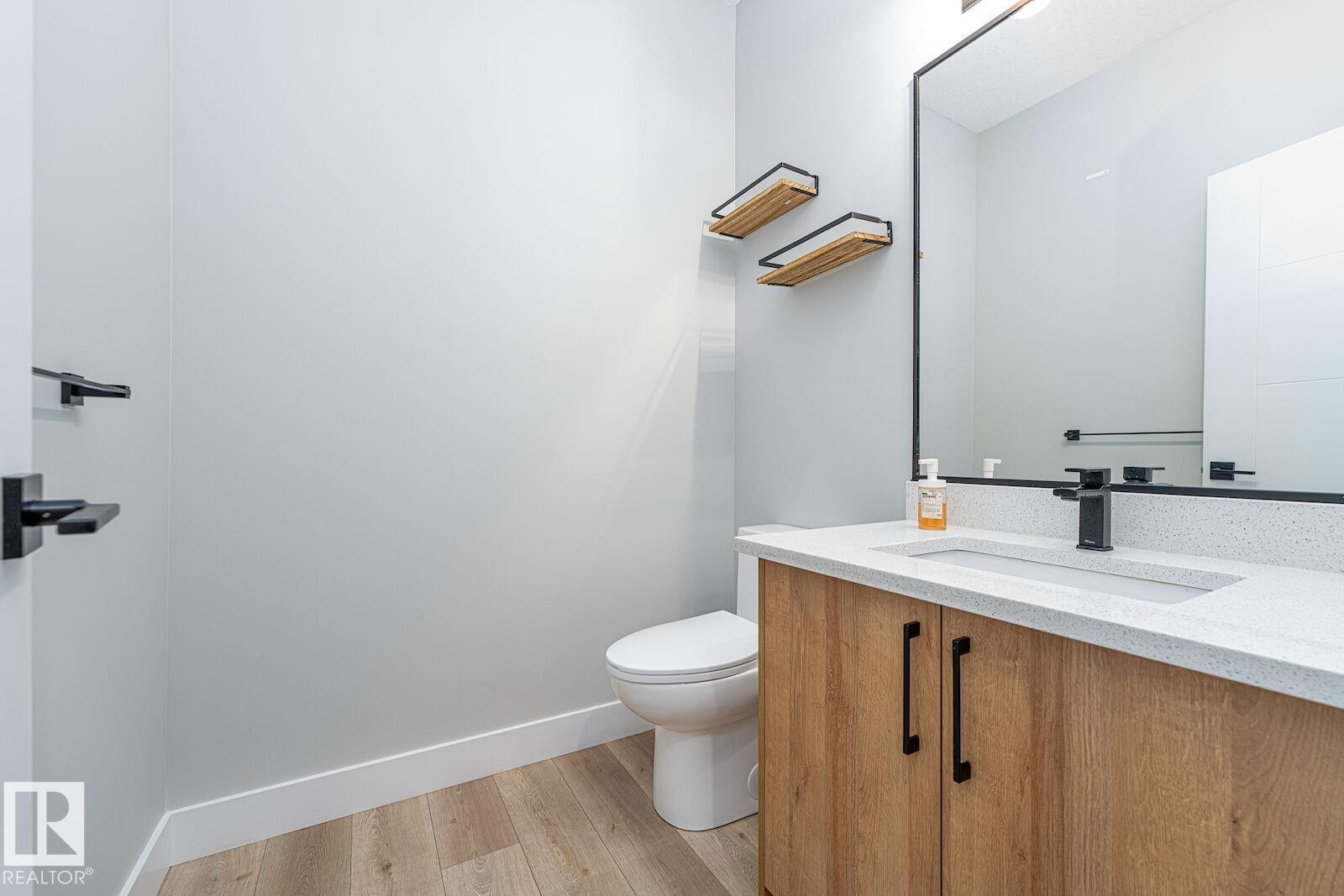 Modern vanity featuring wood-finish cabinetry, a white countertop, and a rectangular undermount sink with a matte black faucet - 17320 9 Avenue, Edmonton, AB