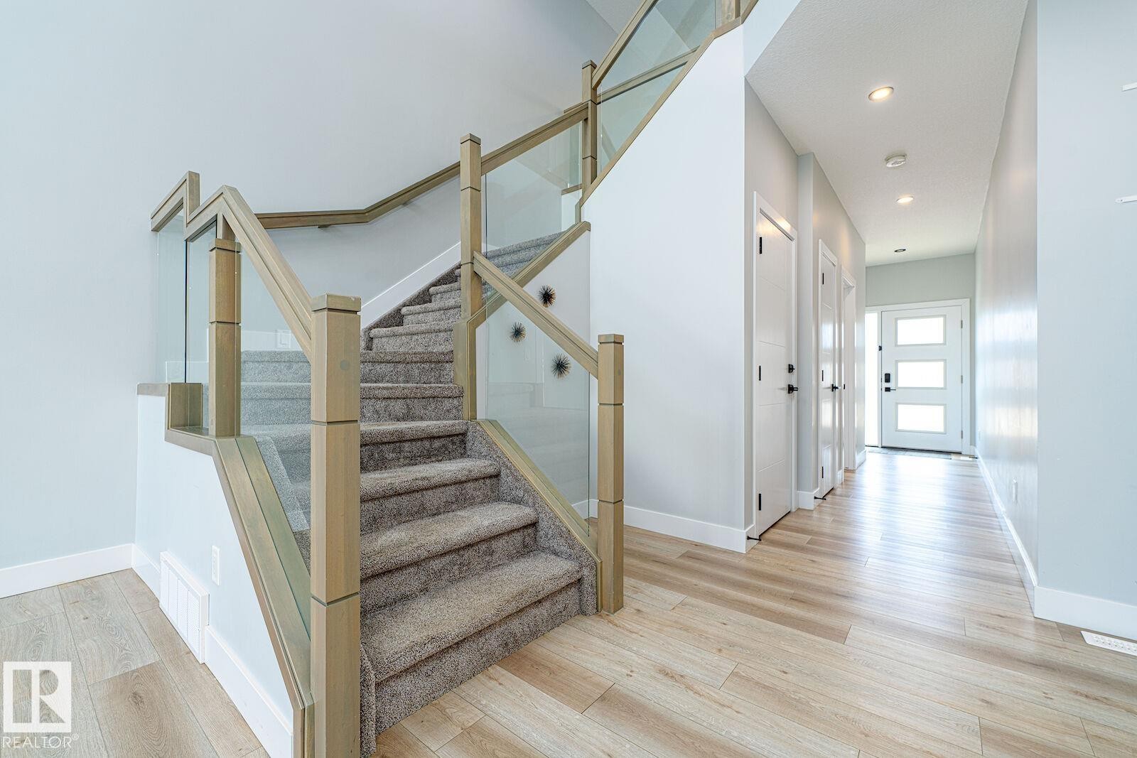 Modern staircase featuring glass panel railings and wood newel posts - 17320 9 Avenue, Edmonton, AB