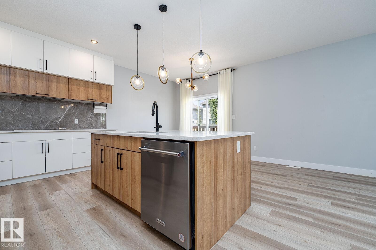 Contemporary kitchen featuring a large central island with a white countertop and integrated stainless steel dishwasher - 17320 9 Avenue, Edmonton, AB