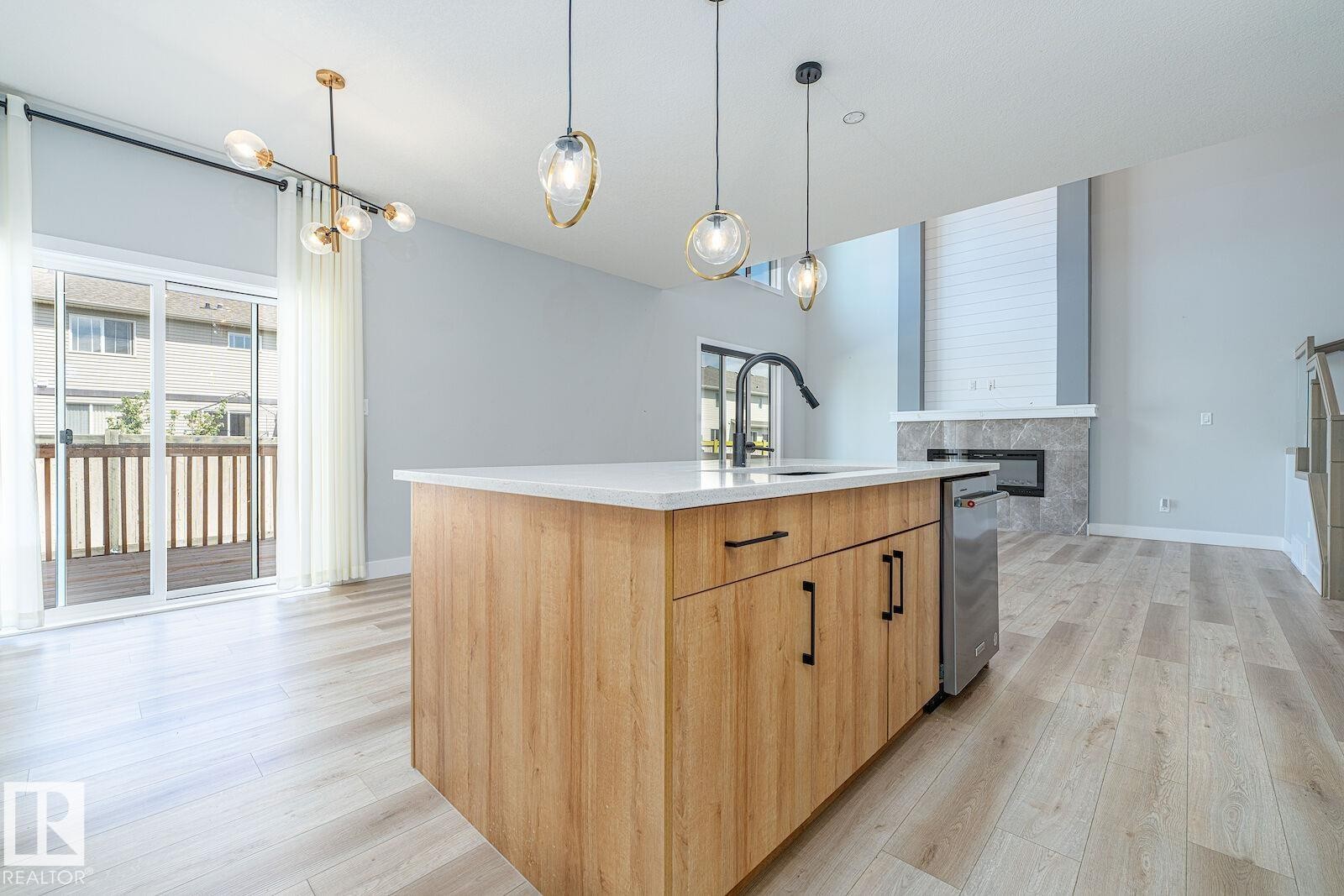 Kitchen island with wood-finish cabinetry, white countertop, integrated sink, and dishwasher - 17320 9 Avenue, Edmonton, AB