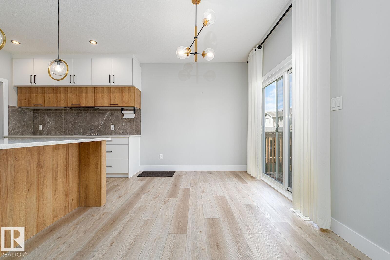 Spacious open-concept area featuring wide plank wood-finish flooring, a contemporary chandelier, and recessed lighting - 17320 9 Avenue, Edmonton, AB
