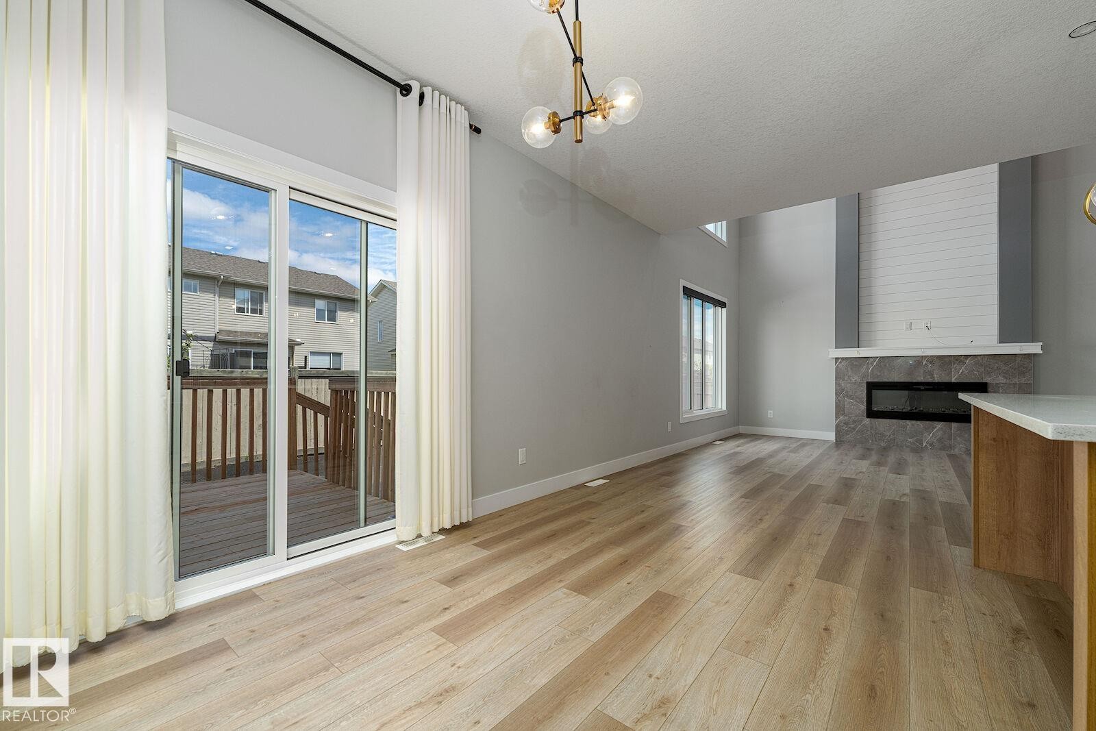 Spacious living area featuring light wood-finish flooring, a contemporary linear fireplace with a stone surround, and a shiplap accent wall - 17320 9 Avenue, Edmonton, AB