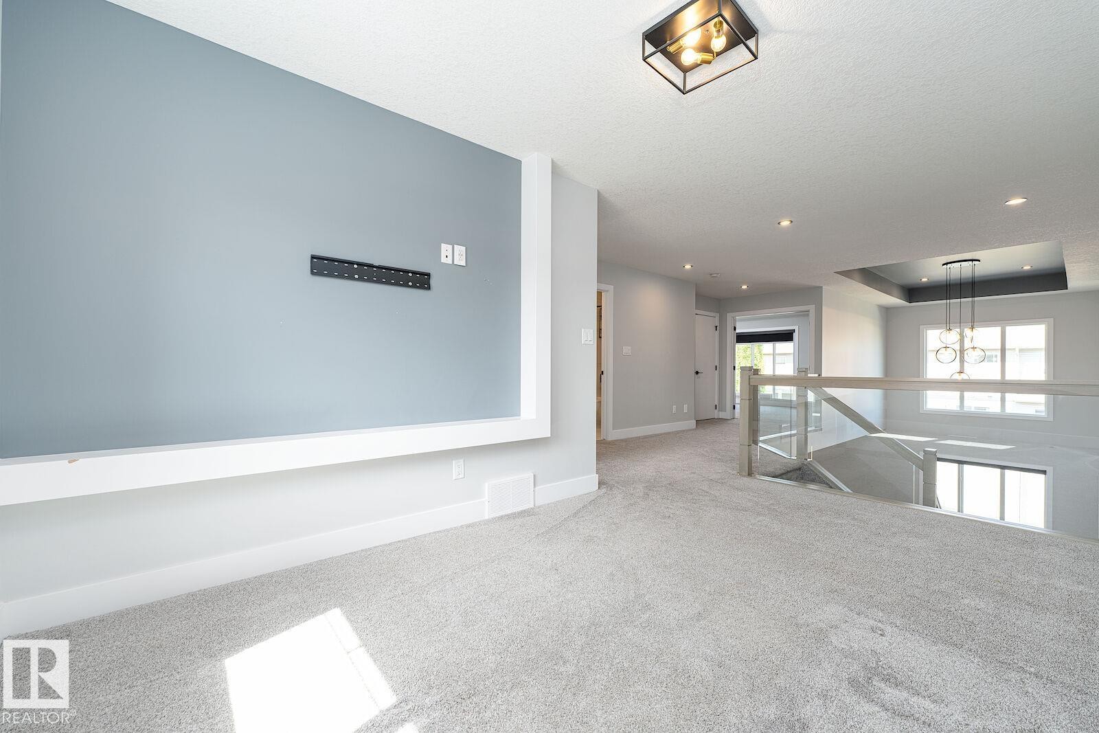 Open landing area featuring light gray carpeting and a built-in media wall with a light blue accent - 17320 9 Avenue, Edmonton, AB