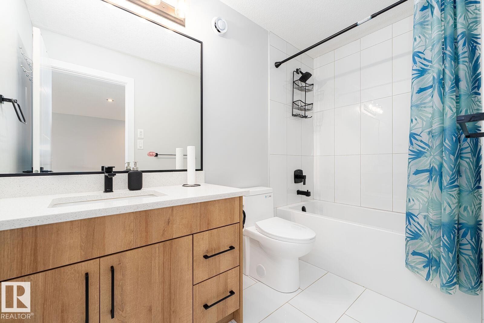 Bathroom featuring a wood-finish vanity with a white countertop and integrated sink, complemented by a matte black faucet - 17320 9 Avenue, Edmonton, AB