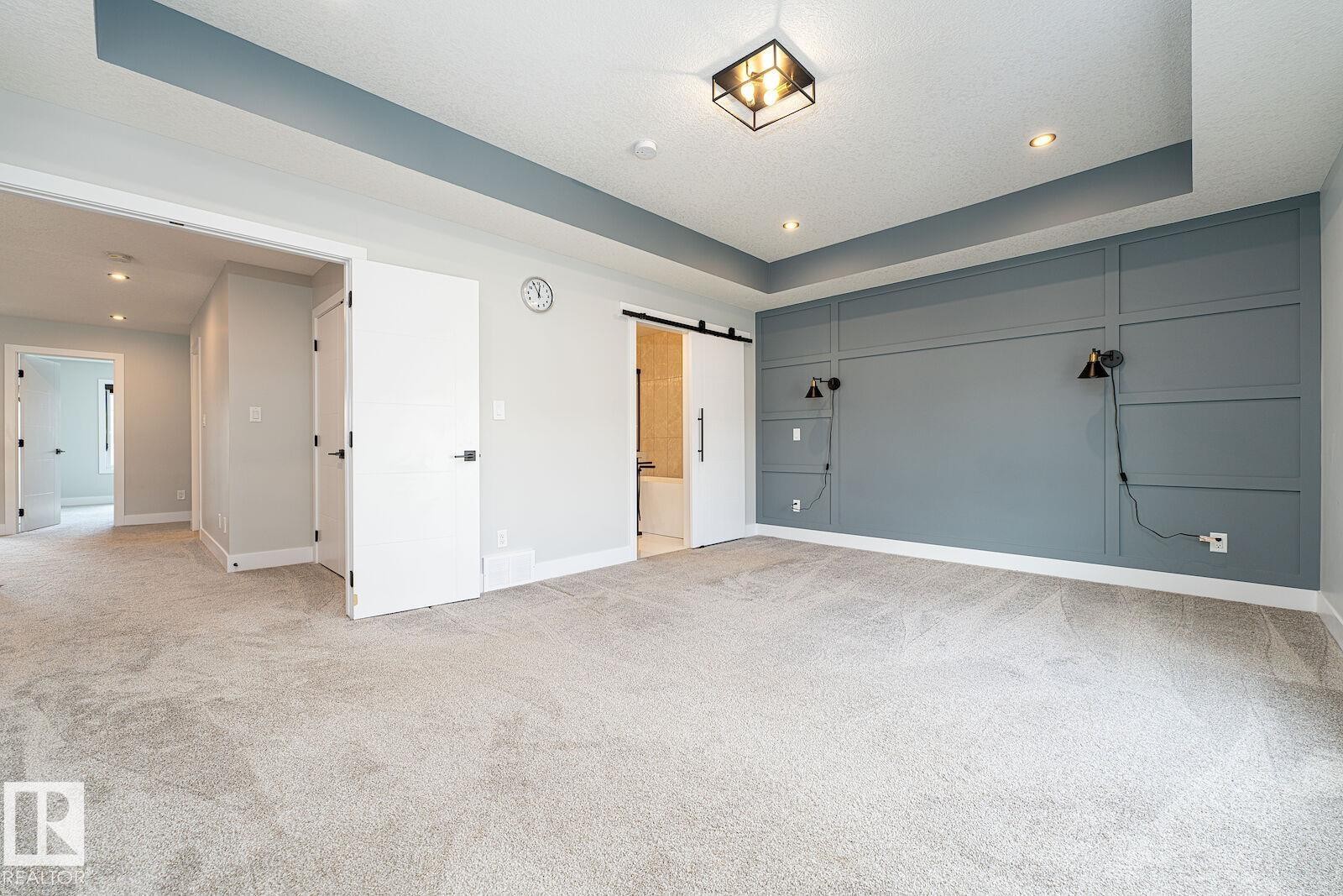 Spacious room featuring a decorative accent wall, tray ceiling, recessed lighting, and soft carpet flooring - 17320 9 Avenue, Edmonton, AB