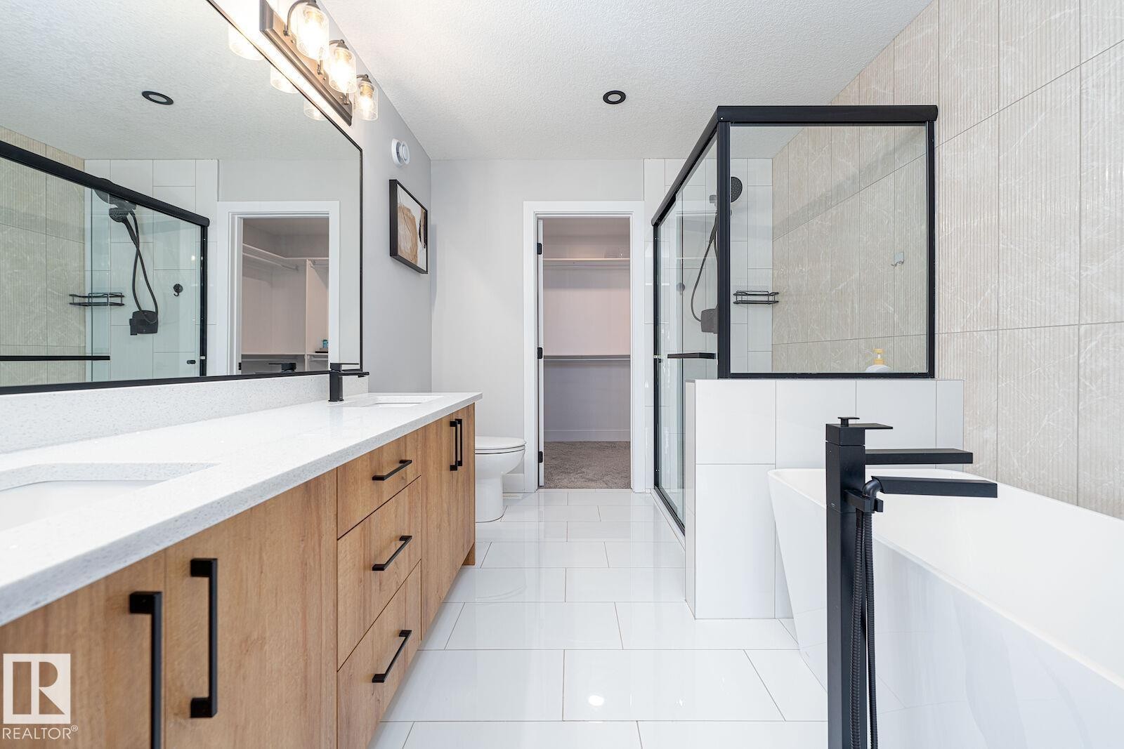 Bathroom featuring a dual vanity with light wood-finish cabinetry, white countertop, and contemporary black hardware - 17320 9 Avenue, Edmonton, AB
