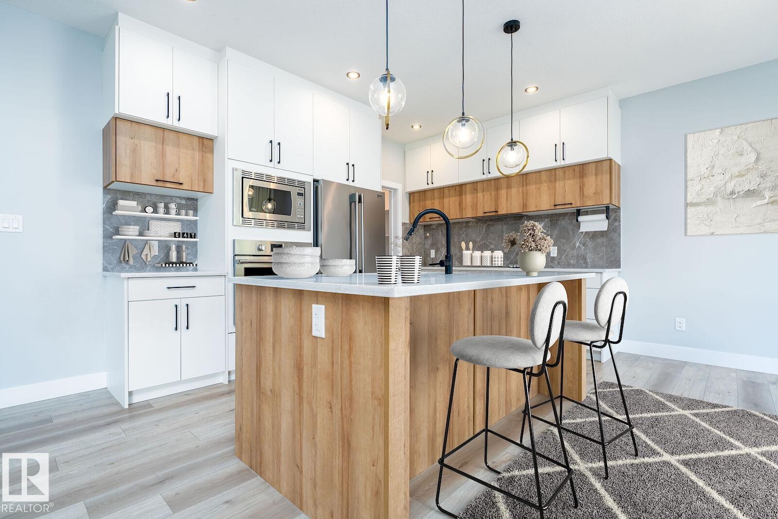 Modern kitchen featuring a light wood-finish island with a white countertop and seating for two - 17320 9 Avenue, Edmonton, AB