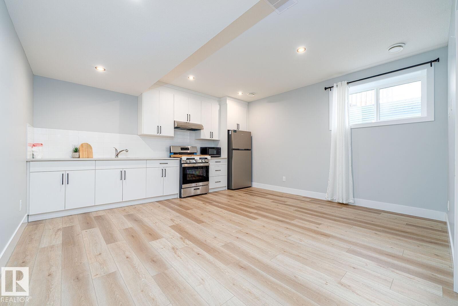 Modern kitchen area featuring white cabinetry, stainless steel appliances, and a light wood-finish flooring - 17320 9 Avenue, Edmonton, AB