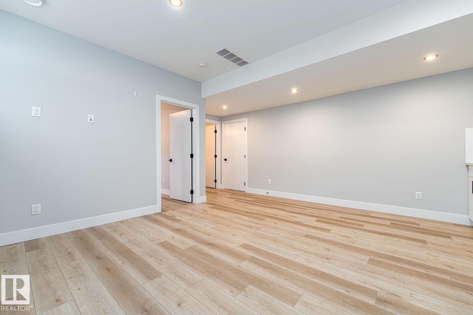 Spacious room featuring light-toned wood-finish flooring, recessed lighting, and crisp white trim - 17320 9 Avenue, Edmonton, AB