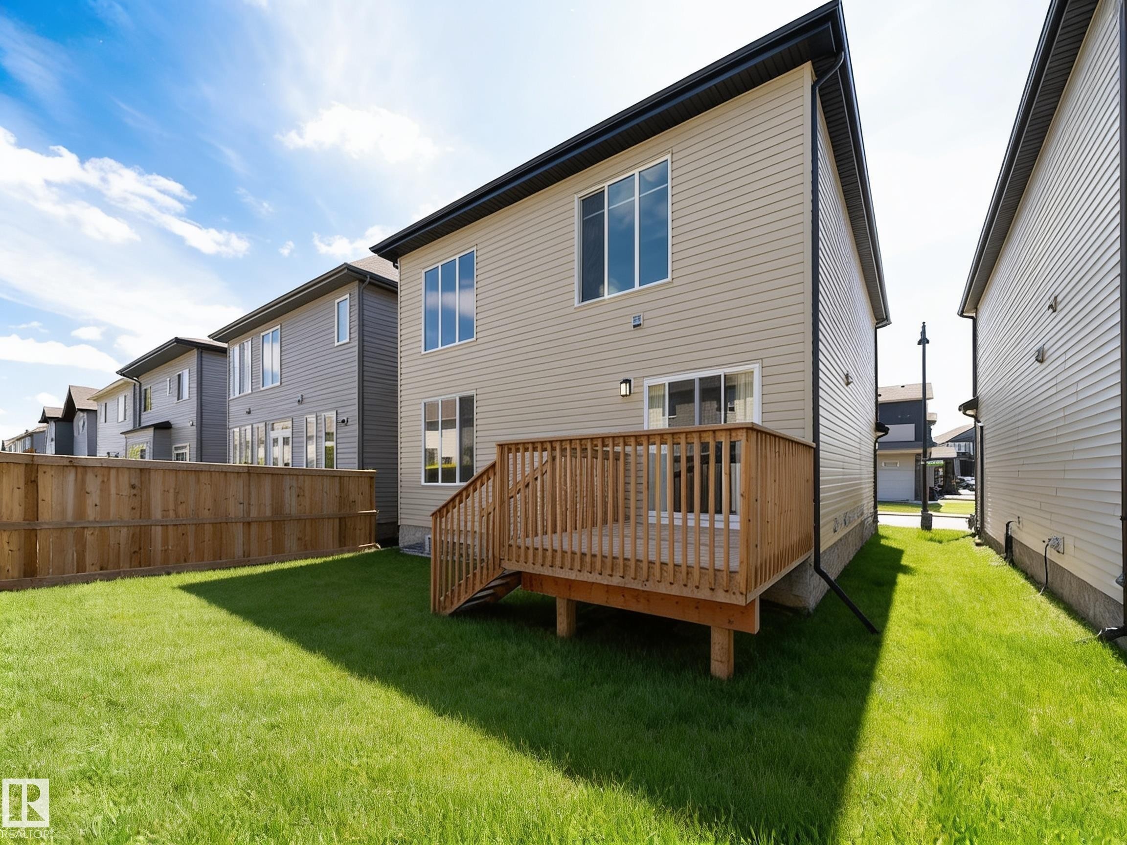 Expansive rear yard featuring a wooden deck with railing, a sliding glass door, and a wooden fence - 17320 9 Avenue, Edmonton, AB