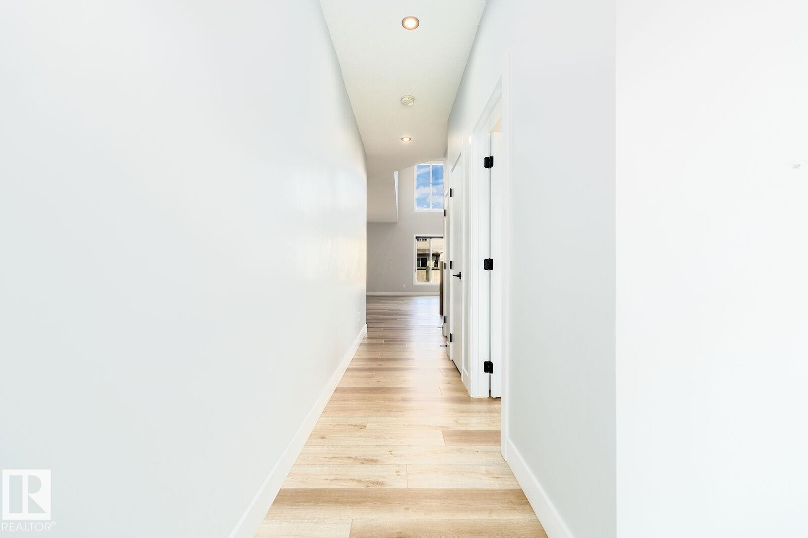 Hallway featuring recessed lighting, wood-finish flooring, white baseboards, and white doors with matte black hardware - 17320 9 Avenue, Edmonton, AB