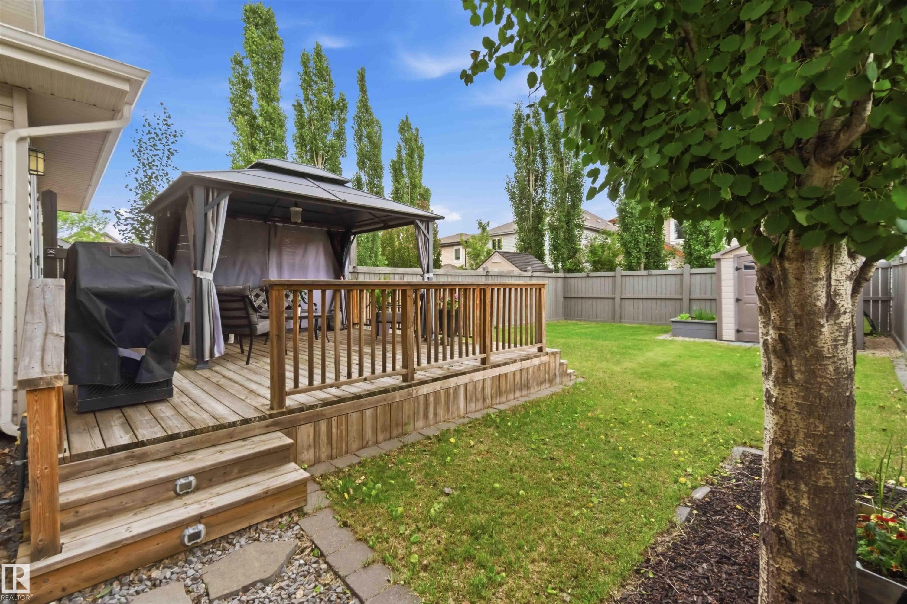 Expansive backyard featuring a wood-finish deck with railing, a detached gazebo structure, a manicured lawn, and a privacy fence - 20013 131 Avenue, Edmonton, AB
