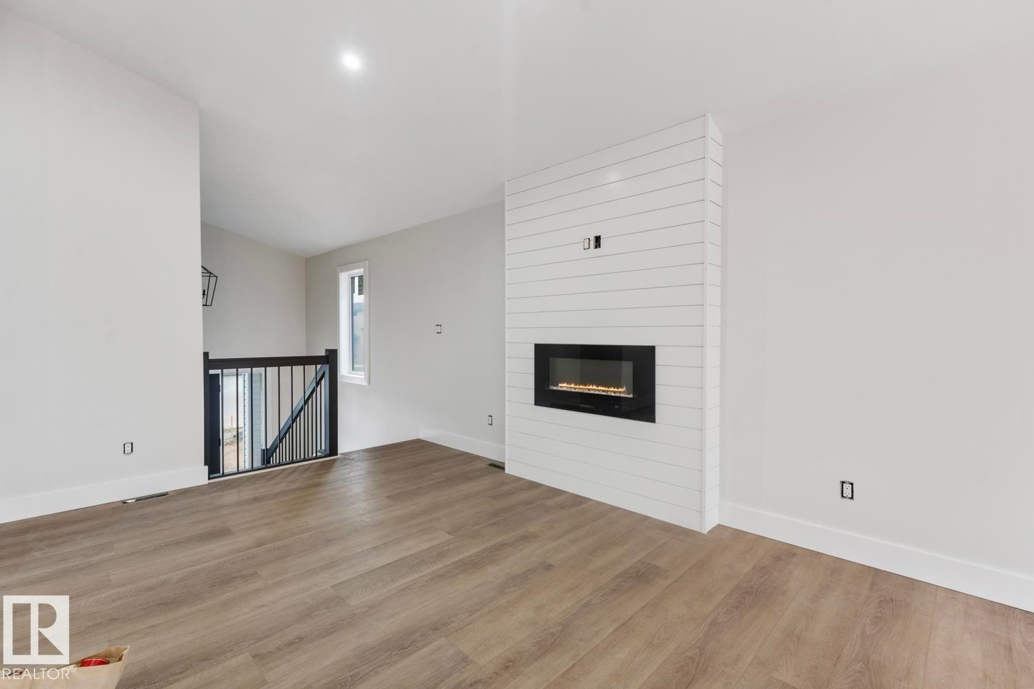 Living area featuring a modern linear fireplace with a shiplap surround, wood-finish flooring, recessed lighting, and a window providing natural light - 301 Fundy Way, Cold Lake, AB - Indoor With Fireplace