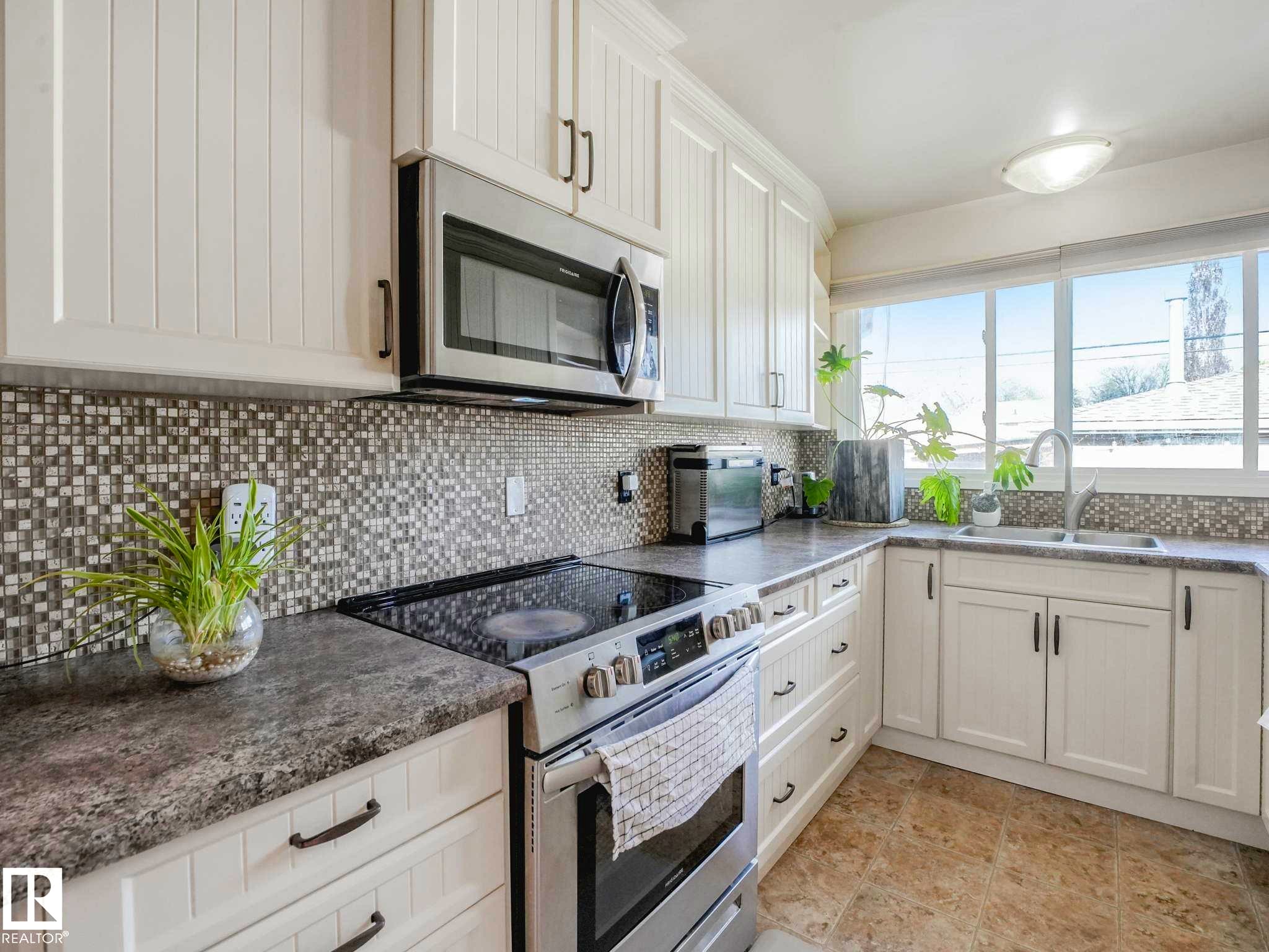 Kitchen featuring white cabinetry, mosaic tile backsplash, solid surface countertops, and a stainless steel over-the-range microwave - 9207 169 Street, Edmonton, AB - Indoor Photo Showing Kitchen With Double Sink With Upgraded Kitchen