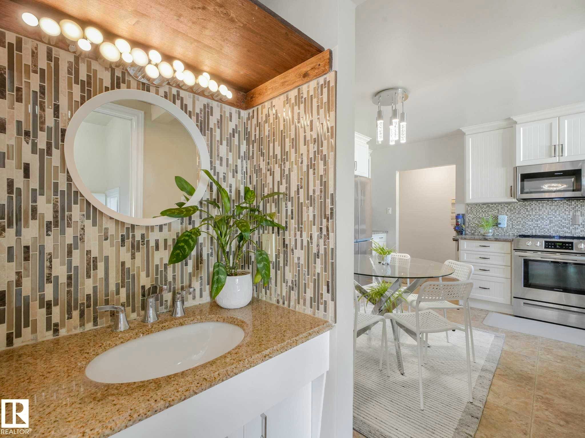 Vanity featuring a mosaic tile backsplash, oval mirror, and a countertop with an integrated sink - 9207 169 Street, Edmonton, AB - Indoor