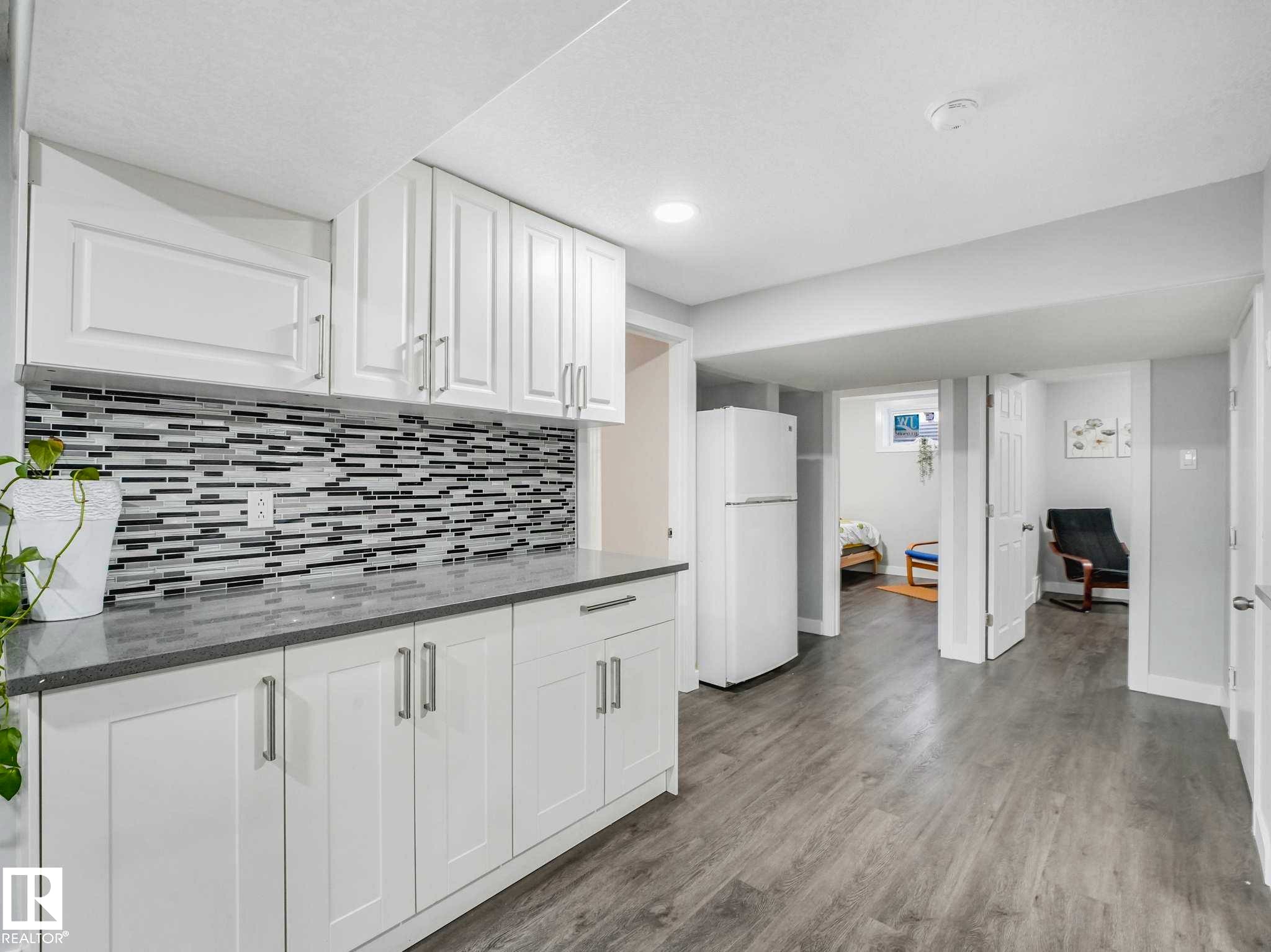 Kitchenette featuring white cabinetry, a mosaic tile backsplash, grey countertops, and wood-finish flooring - 9207 169 Street, Edmonton, AB - Indoor Photo Showing Kitchen