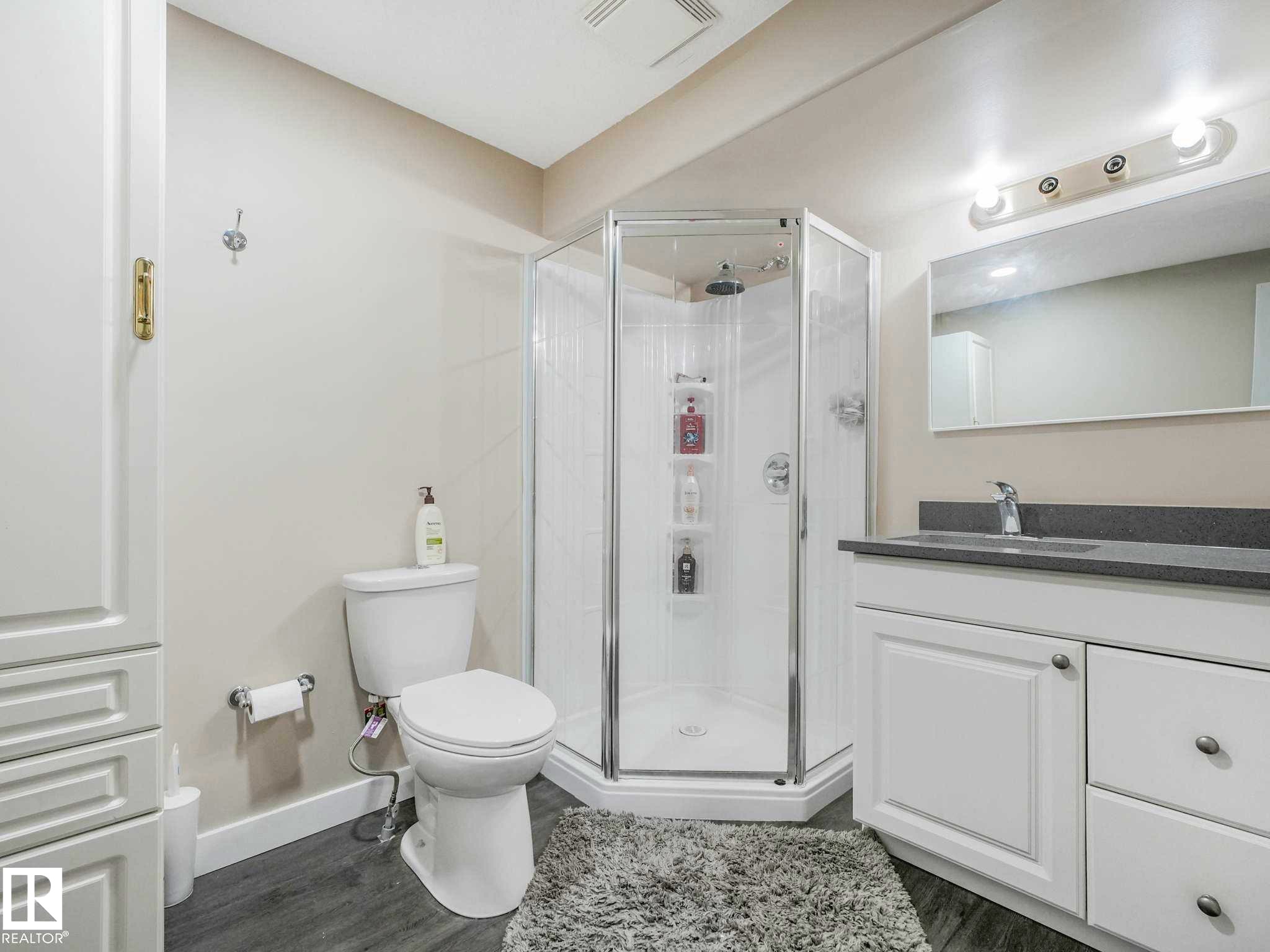 Bathroom featuring a glass-enclosed corner shower, single vanity with a gray countertop, wood-finish flooring, and white cabinetry - 9207 169 Street, Edmonton, AB - Indoor Photo Showing Bathroom