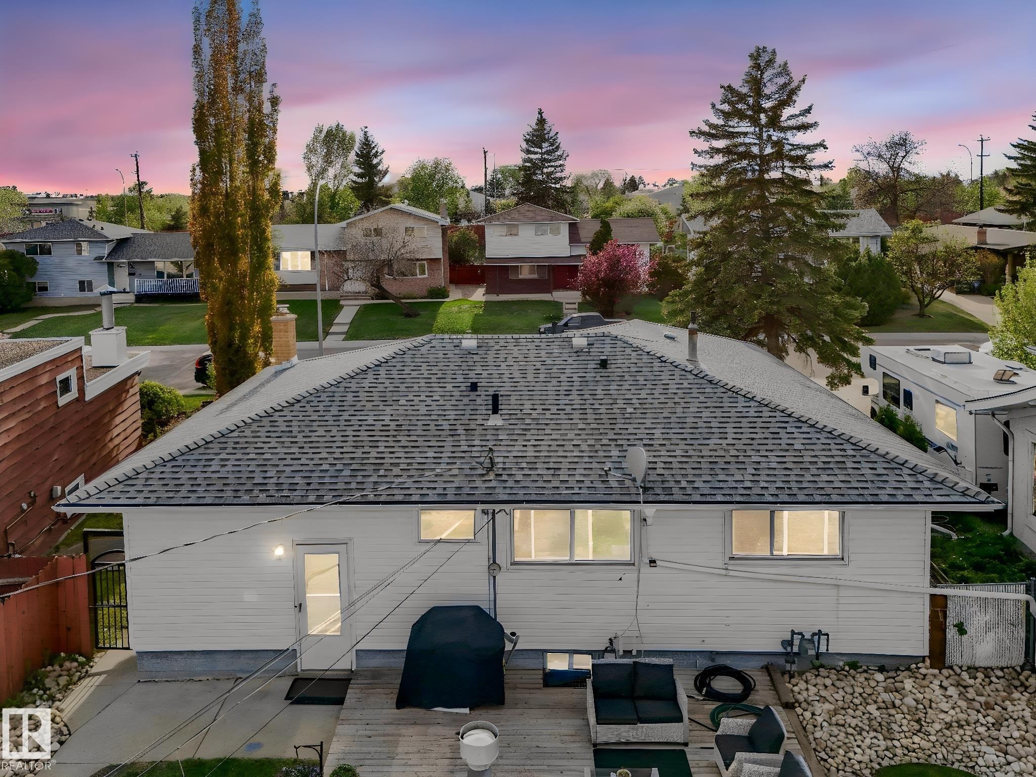 Rear exterior featuring a spacious wooden deck with stone landscaping, white siding, and a shingled roof - 9207 169 Street, Edmonton, AB - Outdoor