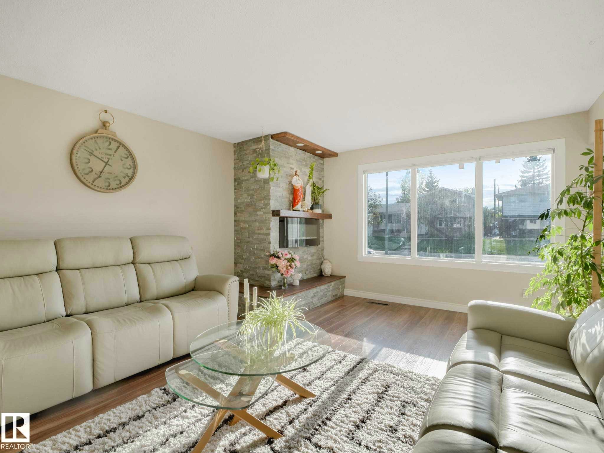 Living area featuring light wood-finish flooring, a stone-clad fireplace with wood mantle, and a large multi-pane window - 9207 169 Street, Edmonton, AB - Indoor Photo Showing Living Room