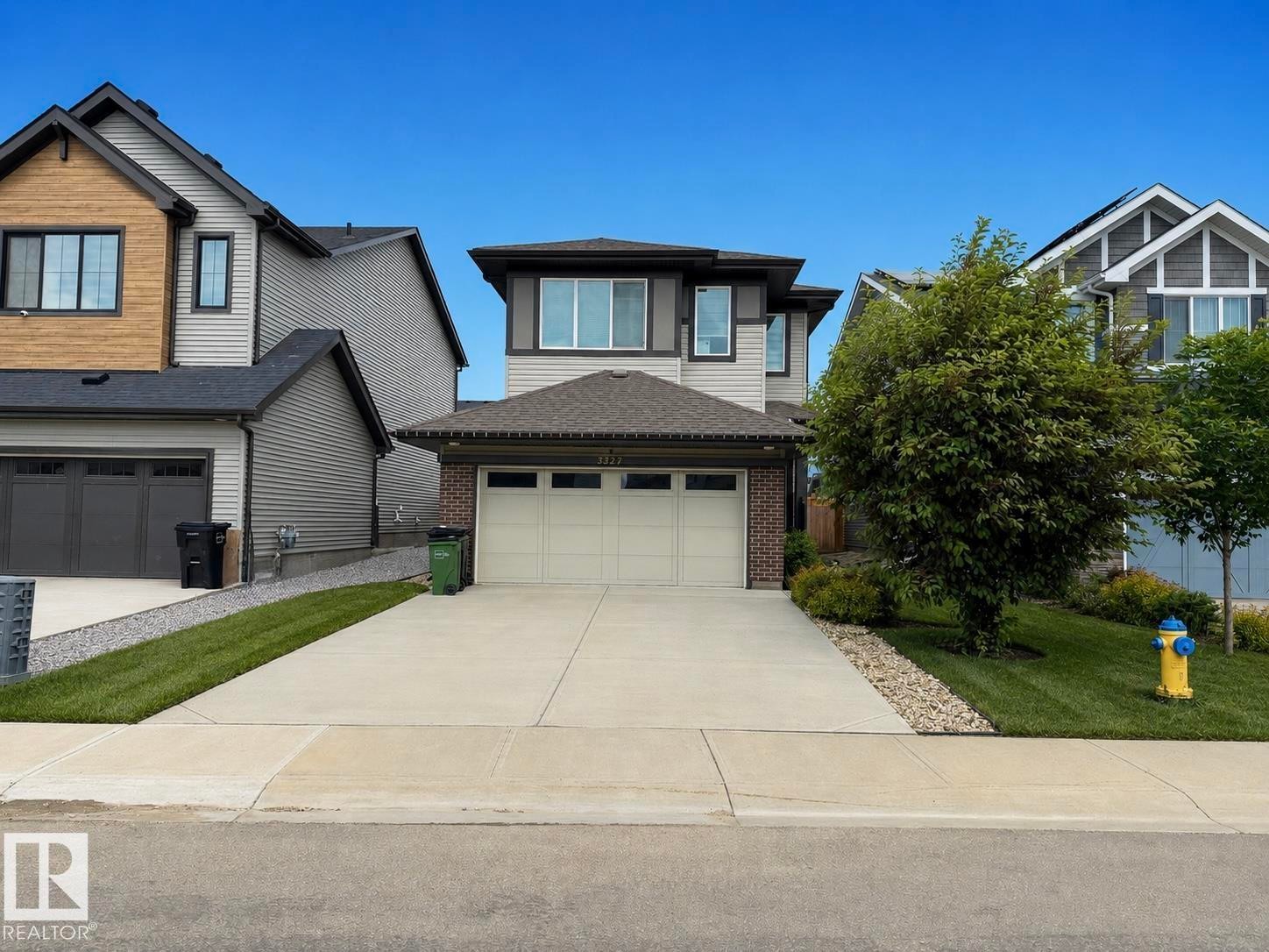 Contemporary exterior featuring a two-car garage, concrete driveway, and a front lawn with mature landscaping - 3234 Chernowski Way, Edmonton, AB