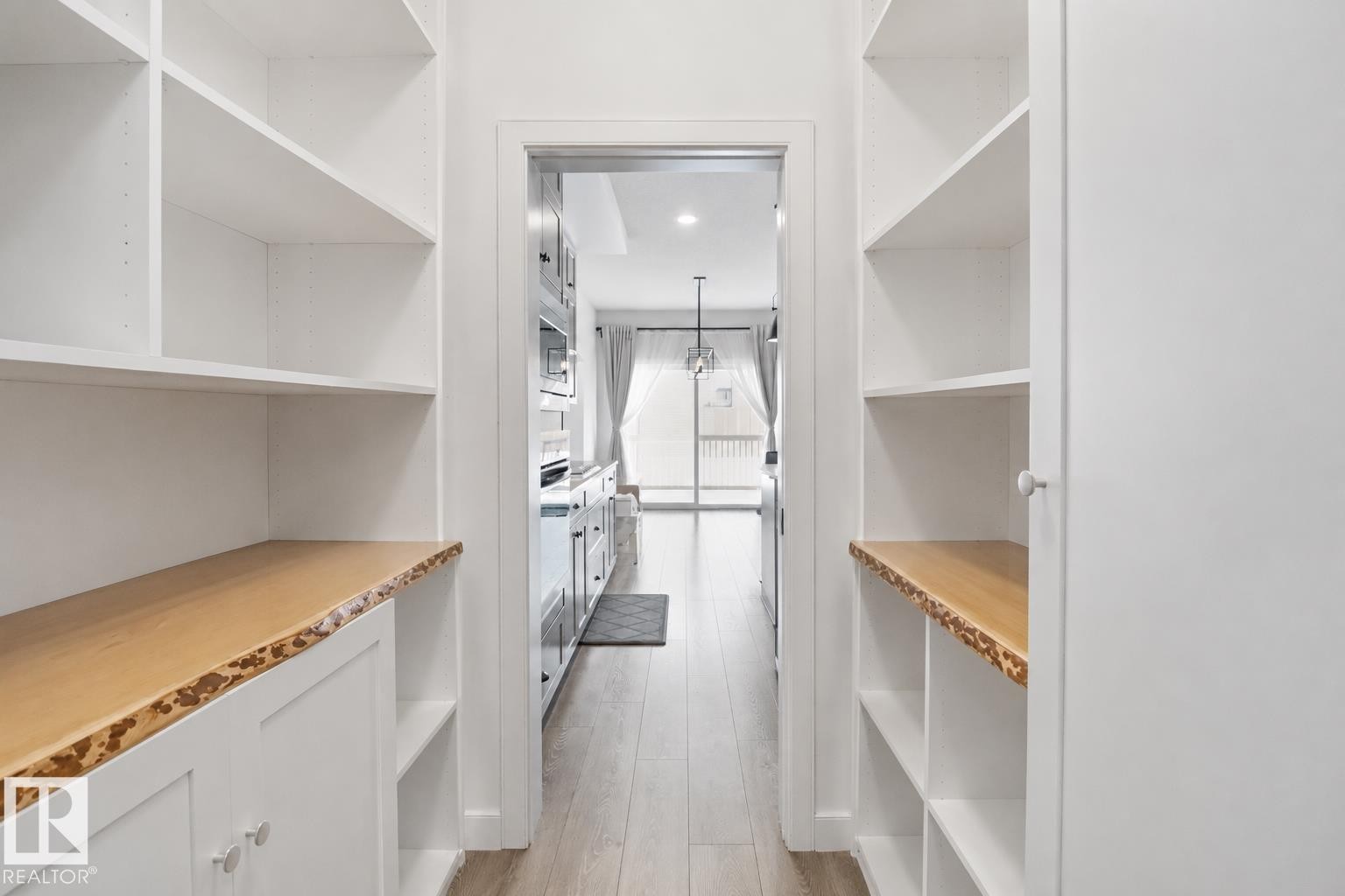 Pantry with extensive white built-in shelving, natural wood-finish countertops featuring live edge detailing, and light wood-finish flooring - 3234 Chernowski Way, Edmonton, AB