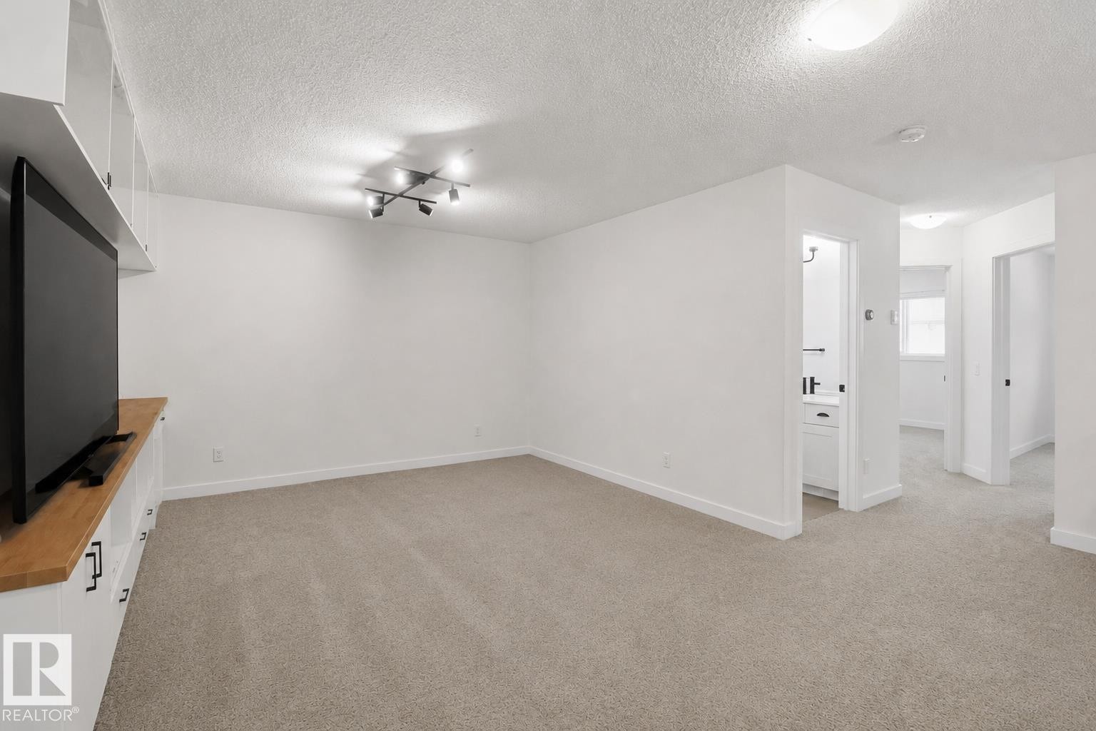Built-in white cabinetry with a wood-finish countertop, track lighting, and soft gray carpeting - 3234 Chernowski Way, Edmonton, AB