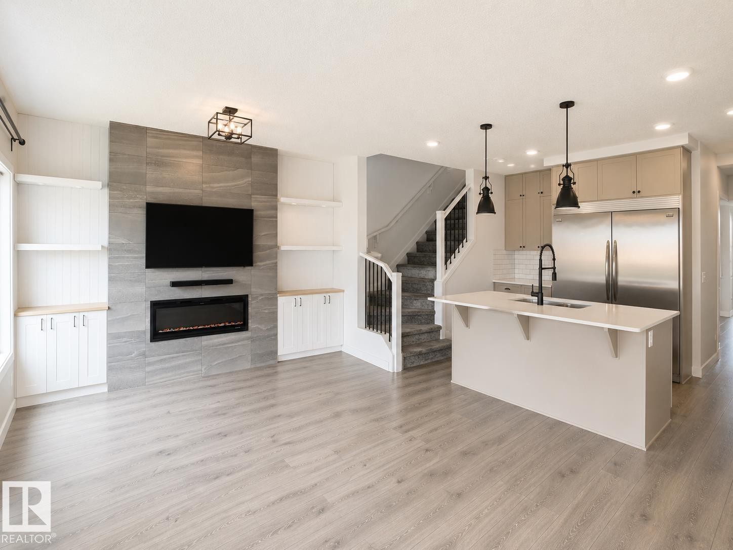 Open-concept living space featuring wood-finish flooring, a contemporary fireplace with a tiled surround, built-in shelving, a kitchen island with pendant lighting, and stainless steel appliances - 3234 Chernowski Way, Edmonton, AB