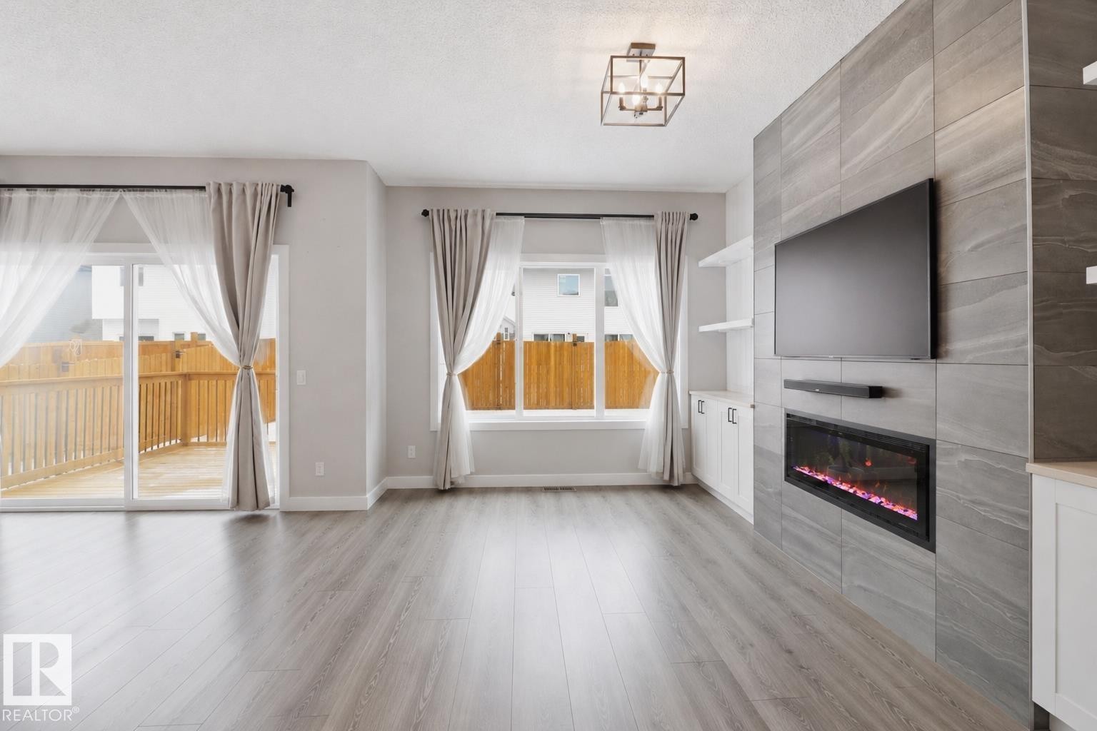 Spacious living area featuring contemporary wood-finish flooring and a tiled media wall with an electric fireplace - 3234 Chernowski Way, Edmonton, AB