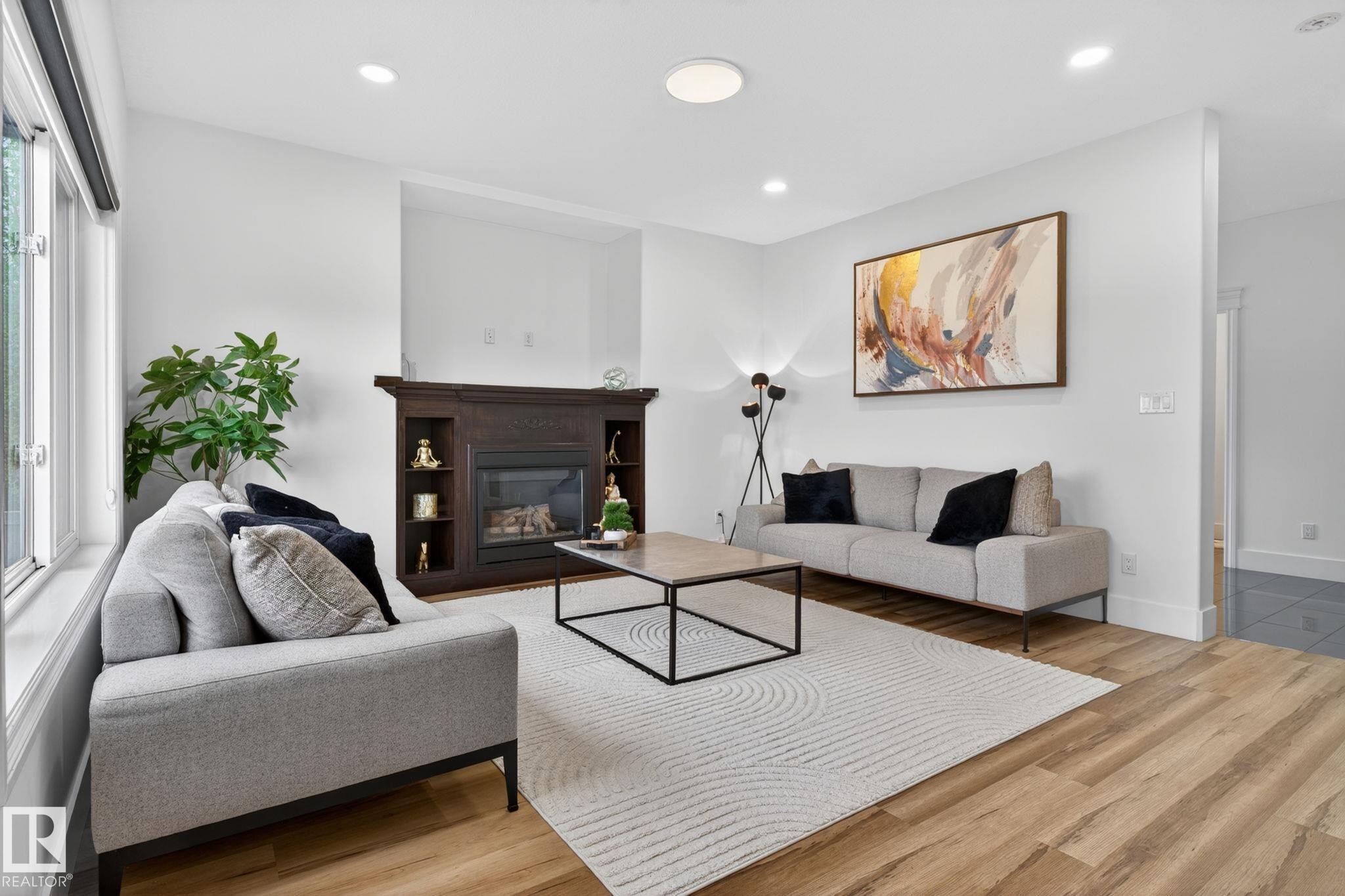 Living area featuring a dark wood-finish fireplace with built-in shelving, wood-finish flooring, recessed lighting, and large windows - 9628 221 Street, Edmonton, AB
