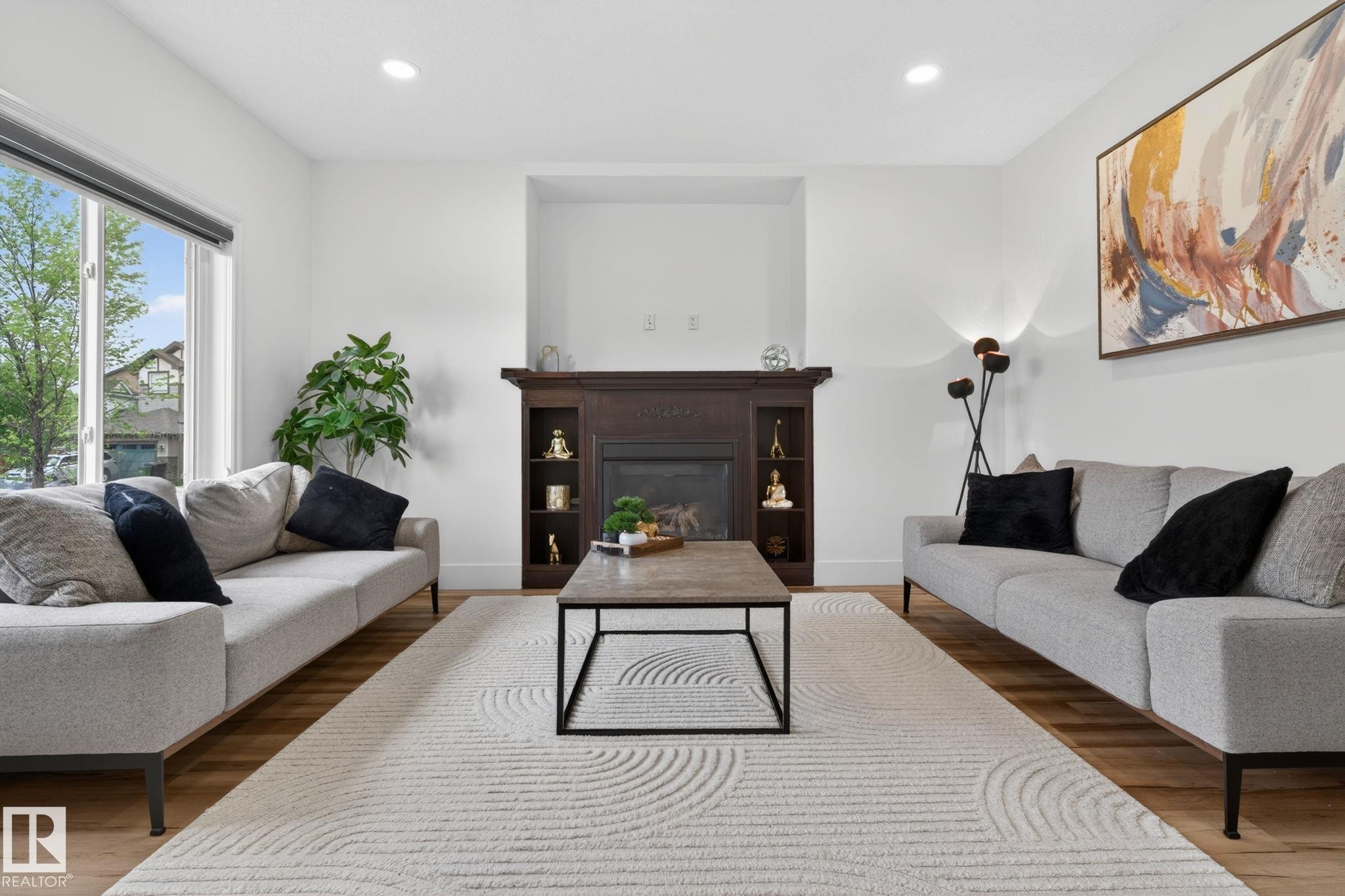 Living area featuring a dark wood fireplace with built-in shelving, recessed ceiling lighting, a large window, and wood-finish flooring - 9628 221 Street, Edmonton, AB