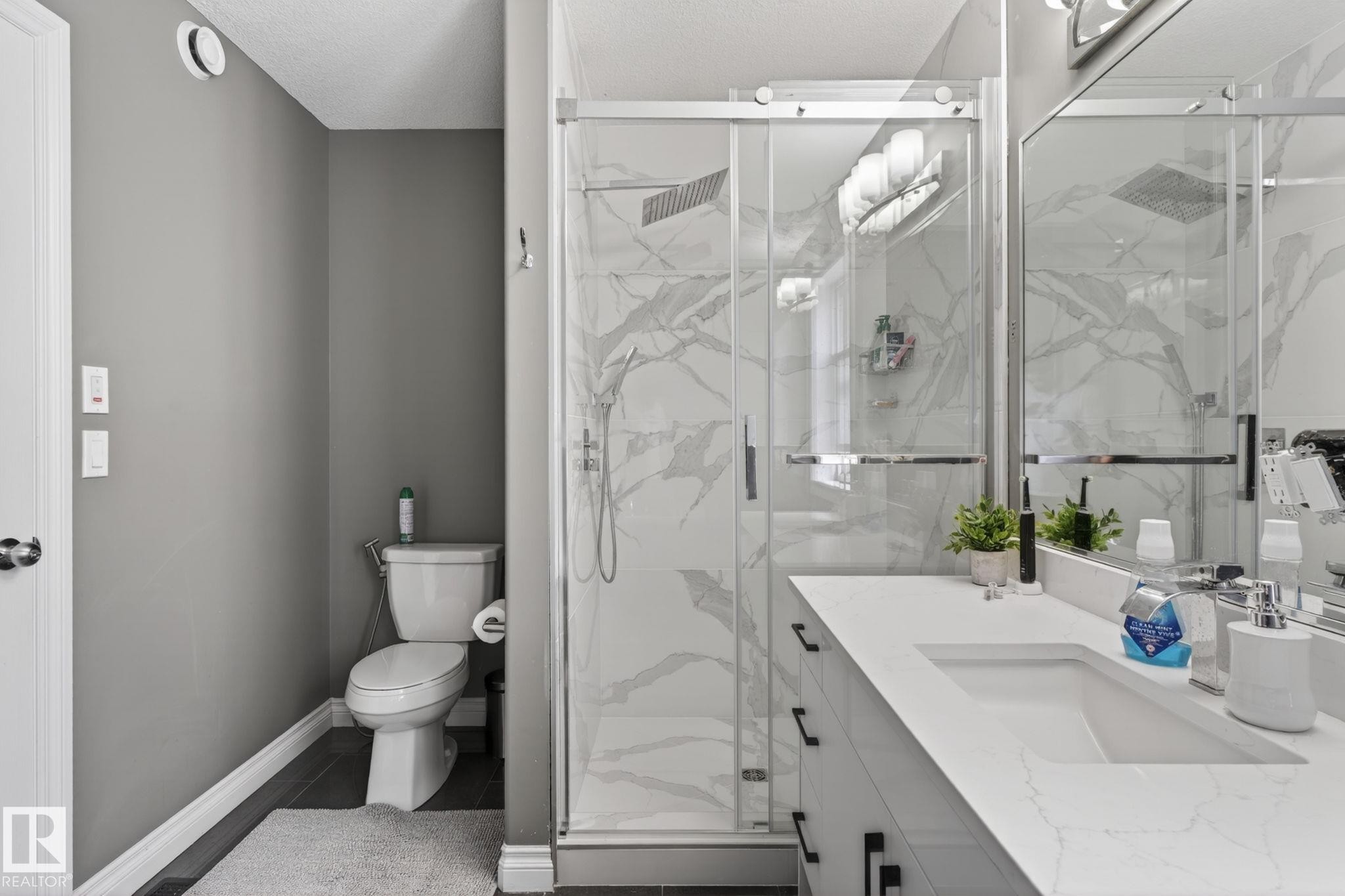 Modern bathroom featuring a glass-enclosed shower with marble-look wall tiling, a single vanity with an integrated rectangular sink, and dark wood-finish flooring - 9628 221 Street, Edmonton, AB