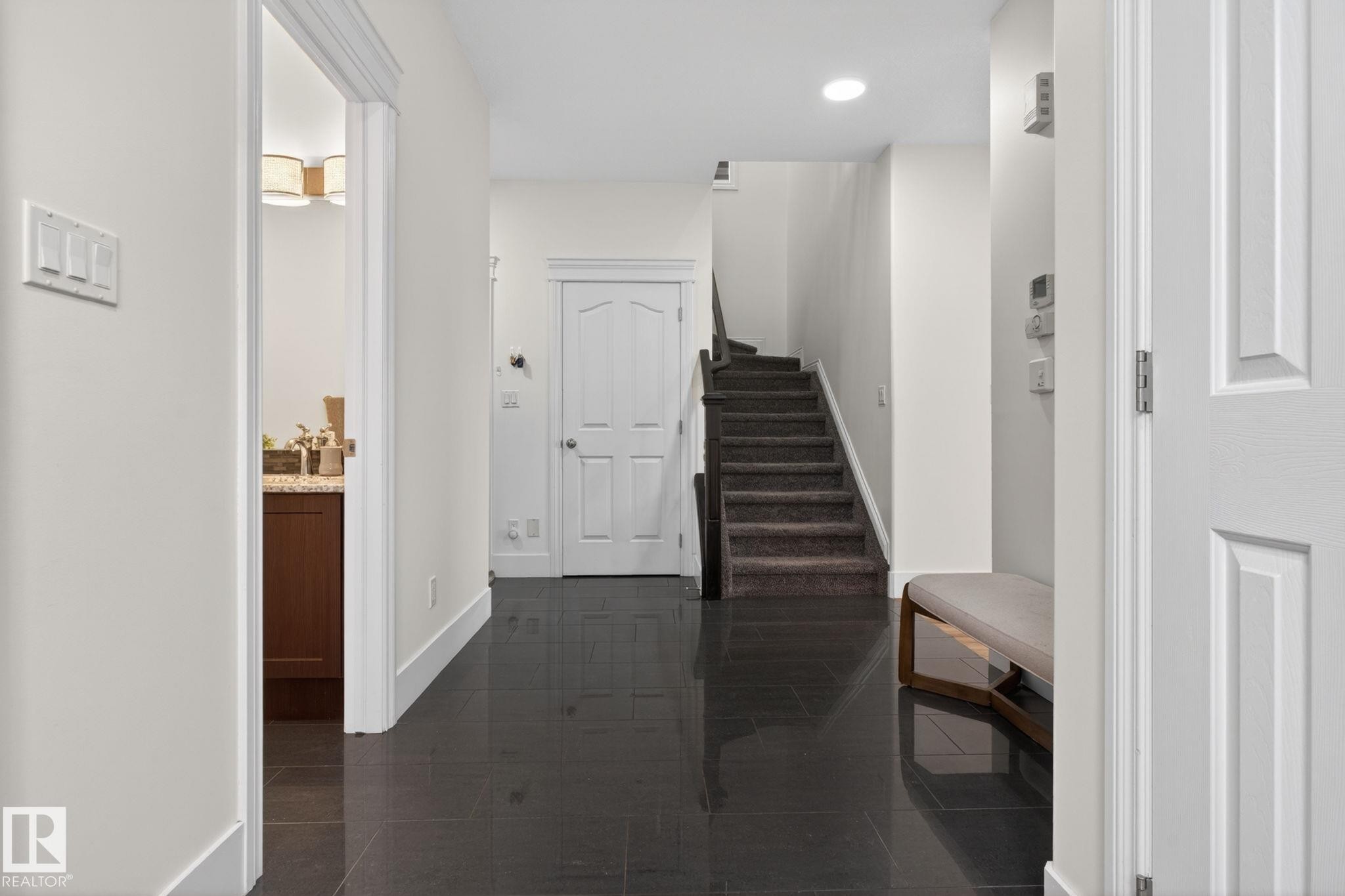 Entryway featuring dark tile flooring, a carpeted staircase, a white paneled door, and recessed lighting - 9628 221 Street, Edmonton, AB