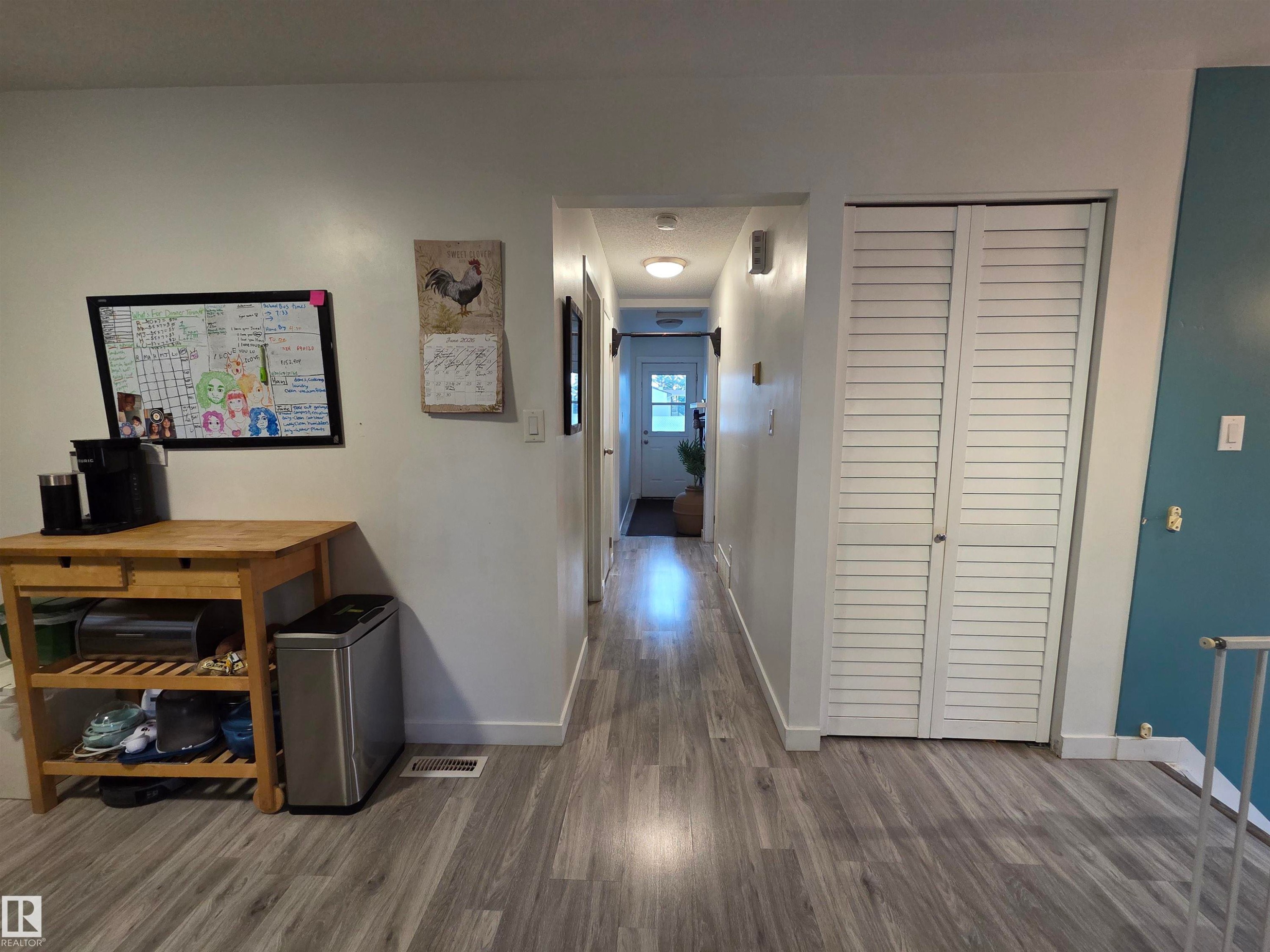 Hallway featuring wood-finish flooring, white walls, and a built-in storage closet with louvered doors - 2514 149 Avenue, Edmonton, AB