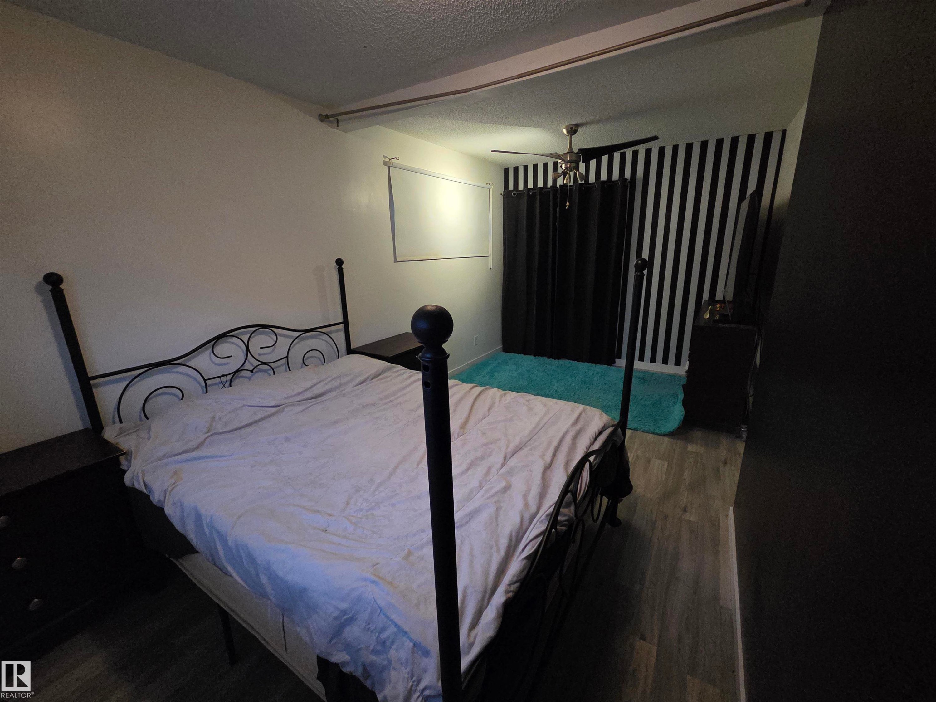 Room featuring wood-finish flooring, a ceiling fan with integrated lighting, and a prominent accent wall with vertical stripes - 2514 149 Avenue, Edmonton, AB