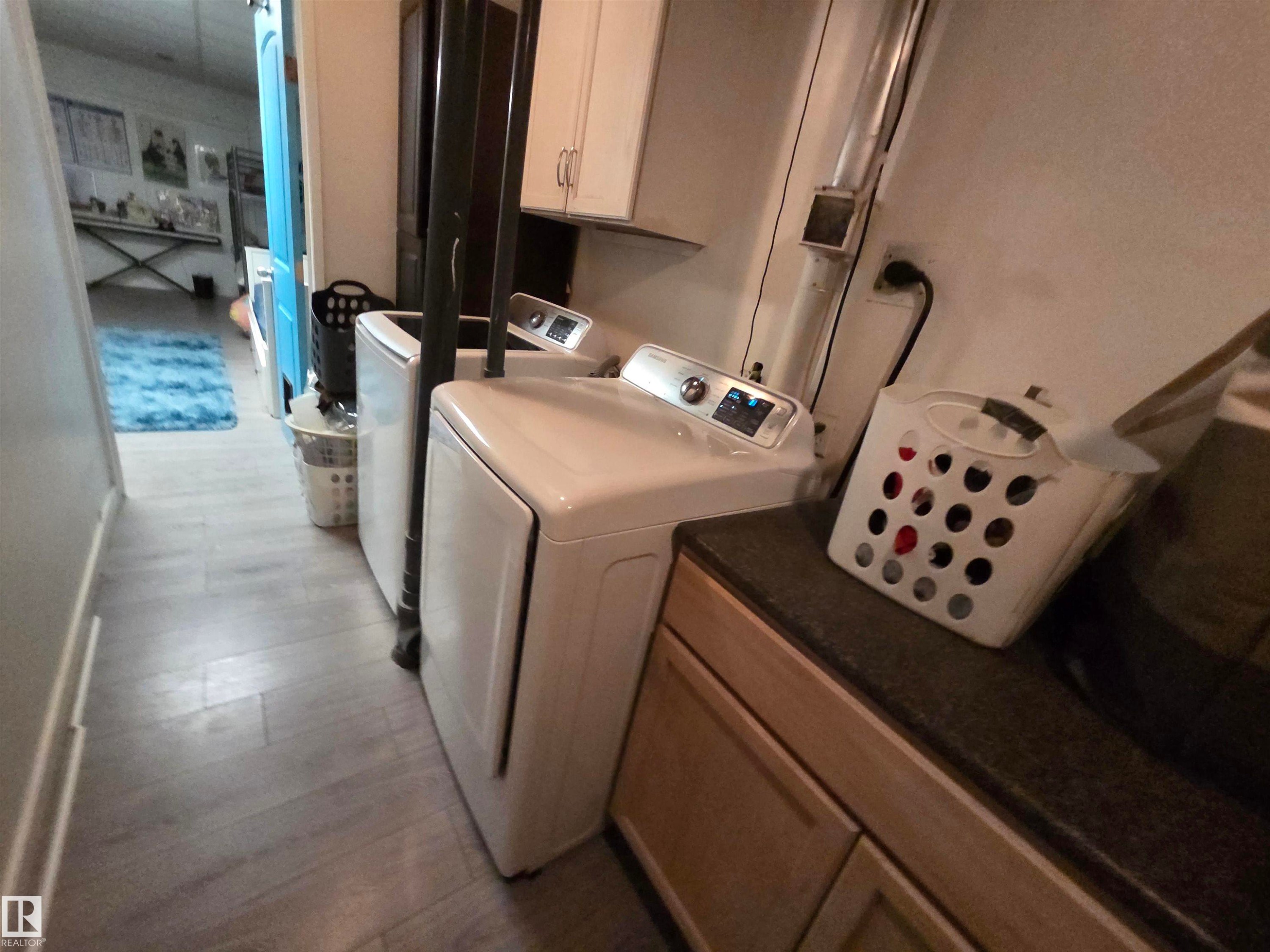 Dedicated laundry area featuring a washer and dryer, light wood-finish flooring, and cabinetry with dark countertops - 2514 149 Avenue, Edmonton, AB