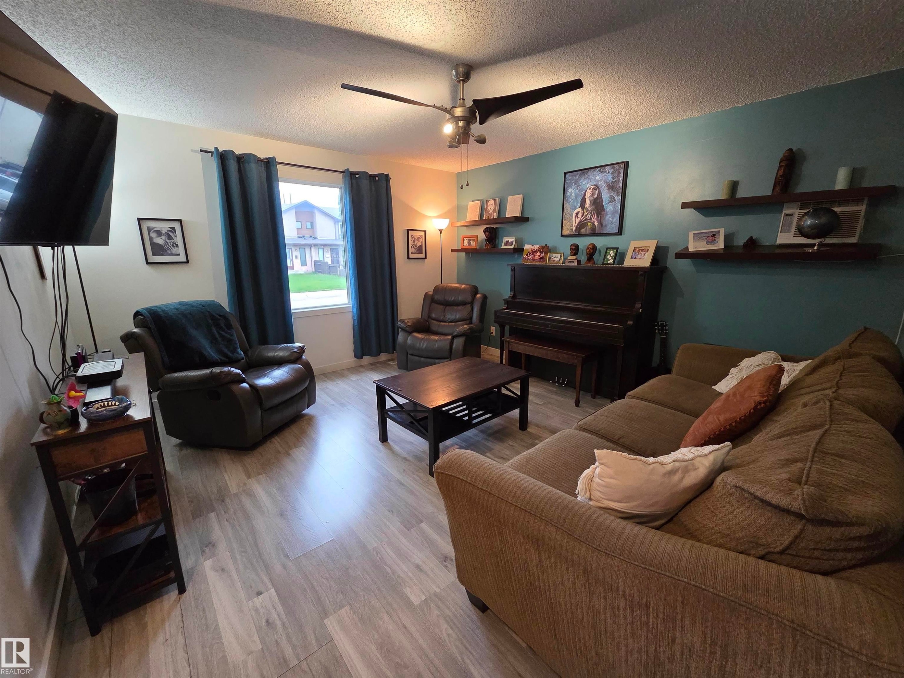 Living area featuring wood-finish flooring, a ceiling fan with integrated lighting, and built-in floating shelves - 2514 149 Avenue, Edmonton, AB