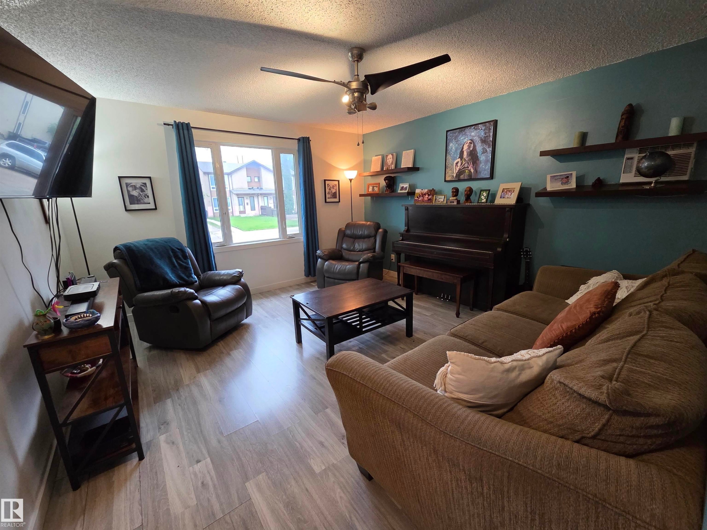 Spacious living area featuring wood-finish flooring, a ceiling fan with integrated lighting, and a prominent window - 2514 149 Avenue, Edmonton, AB