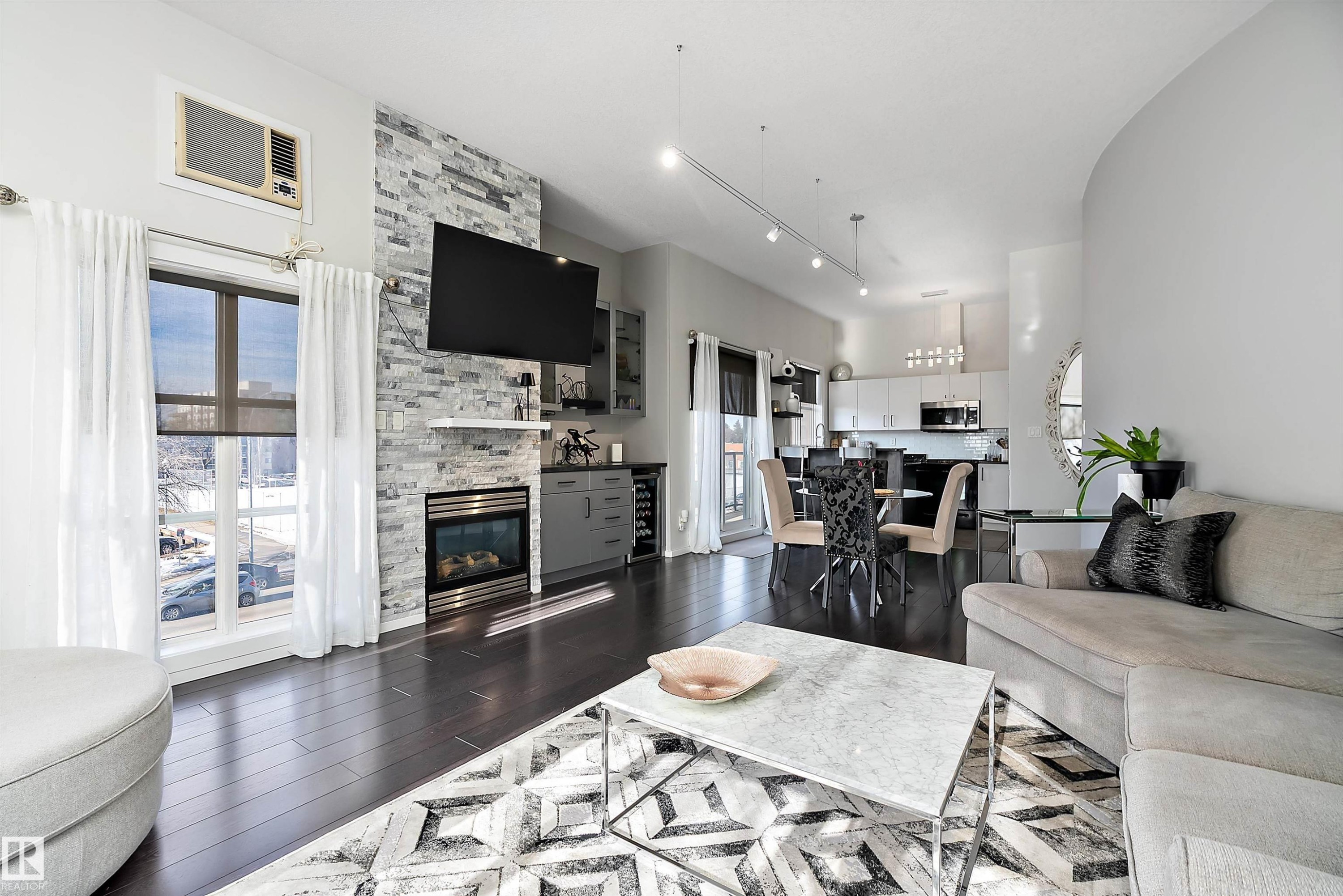 Living room with dark wood finished floors, a fireplace, rail lighting, and beverage cooler - 302 10905 109 Street, Edmonton, AB