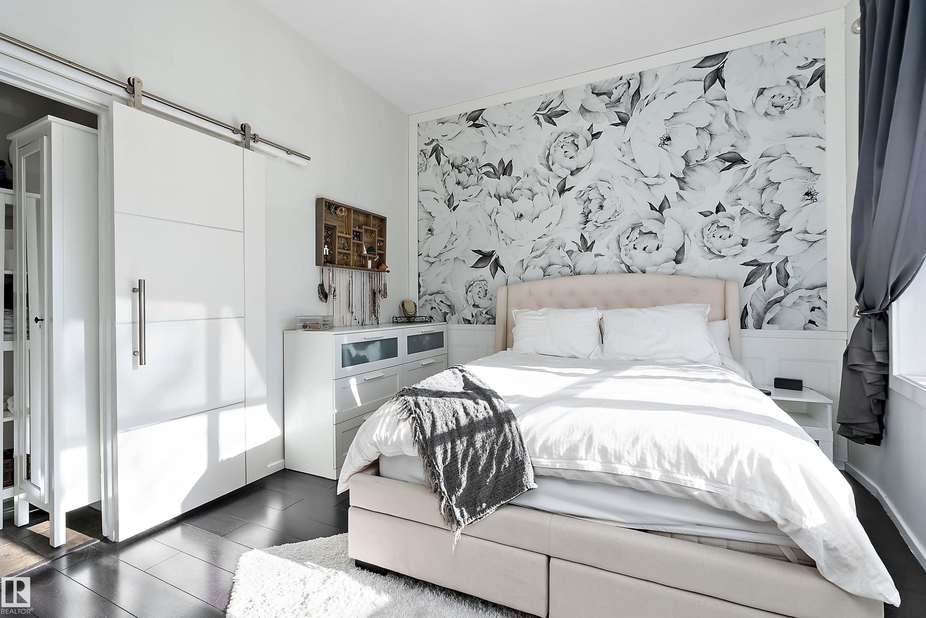 Bedroom featuring a barn door, wood finished floors, an accent wall, and wallpapered walls - 302 10905 109 Street, Edmonton, AB