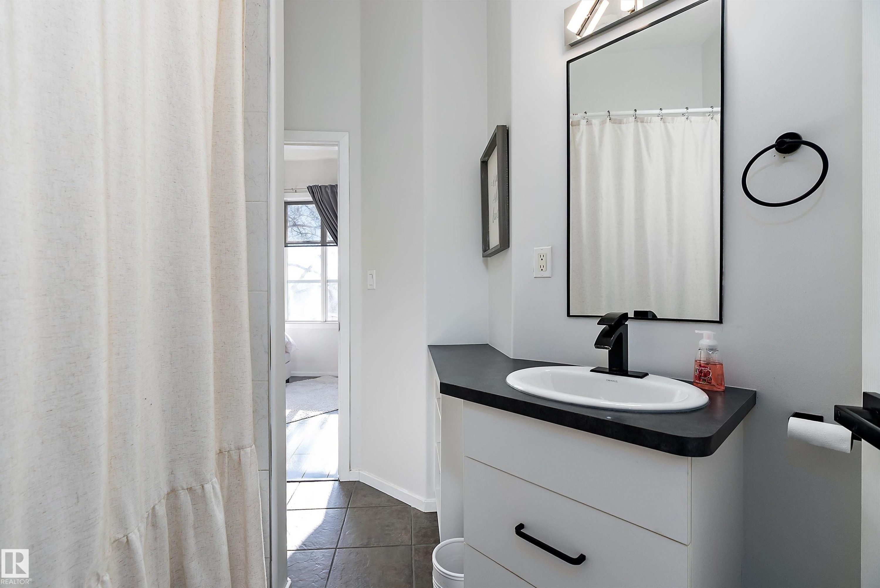 Full bath with vanity, a shower with shower curtain, and dark tile patterned floors - 302 10905 109 Street, Edmonton, AB