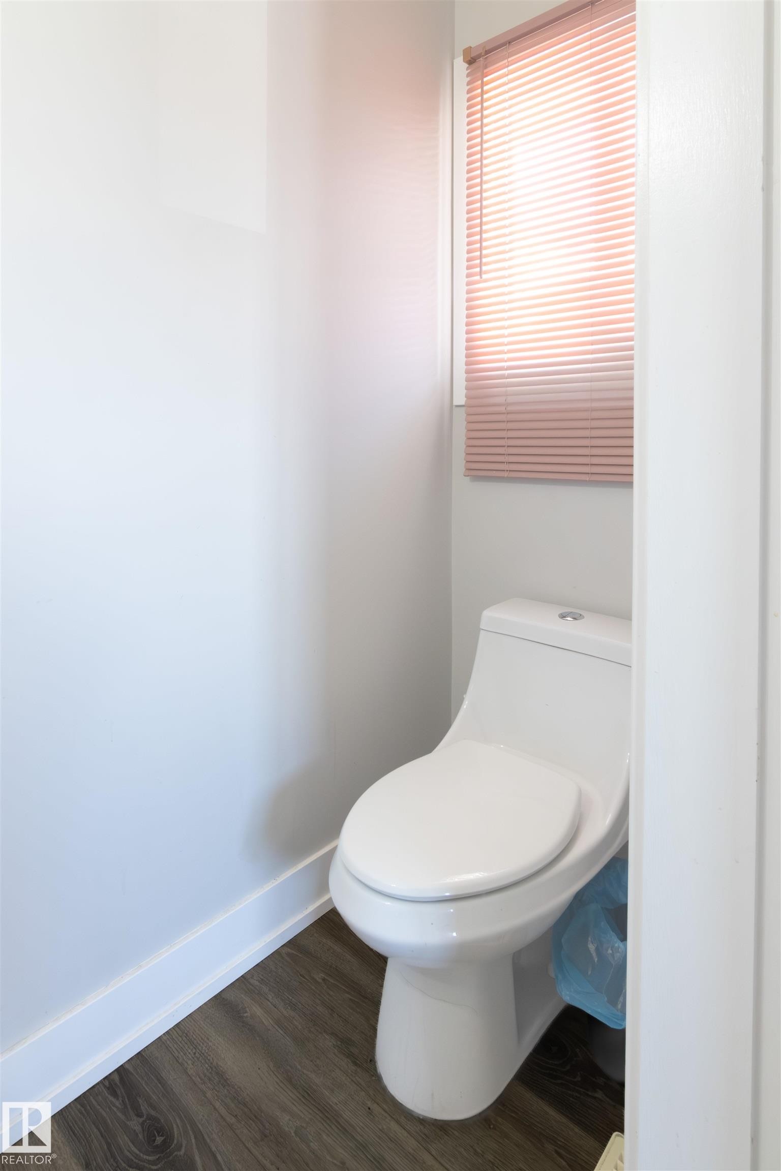 Compact water closet with a white toilet, wood-finish flooring, and a window with blinds - 7115 39A Avenue, Edmonton, AB - Indoor Photo Showing Bathroom