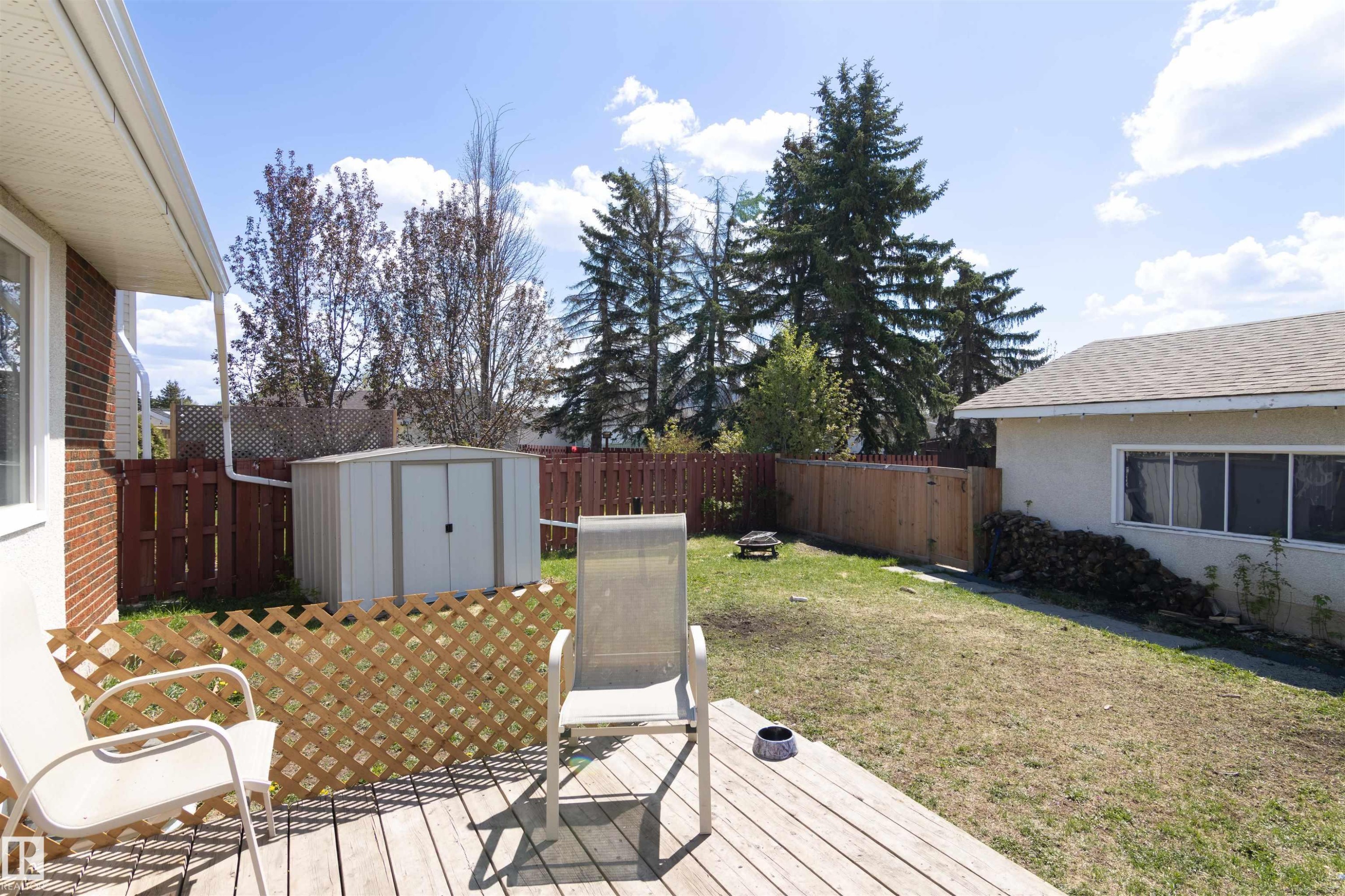 Decked backyard space with a storage shed, wood privacy fence, and mature trees - 7115 39A Avenue, Edmonton, AB - Outdoor