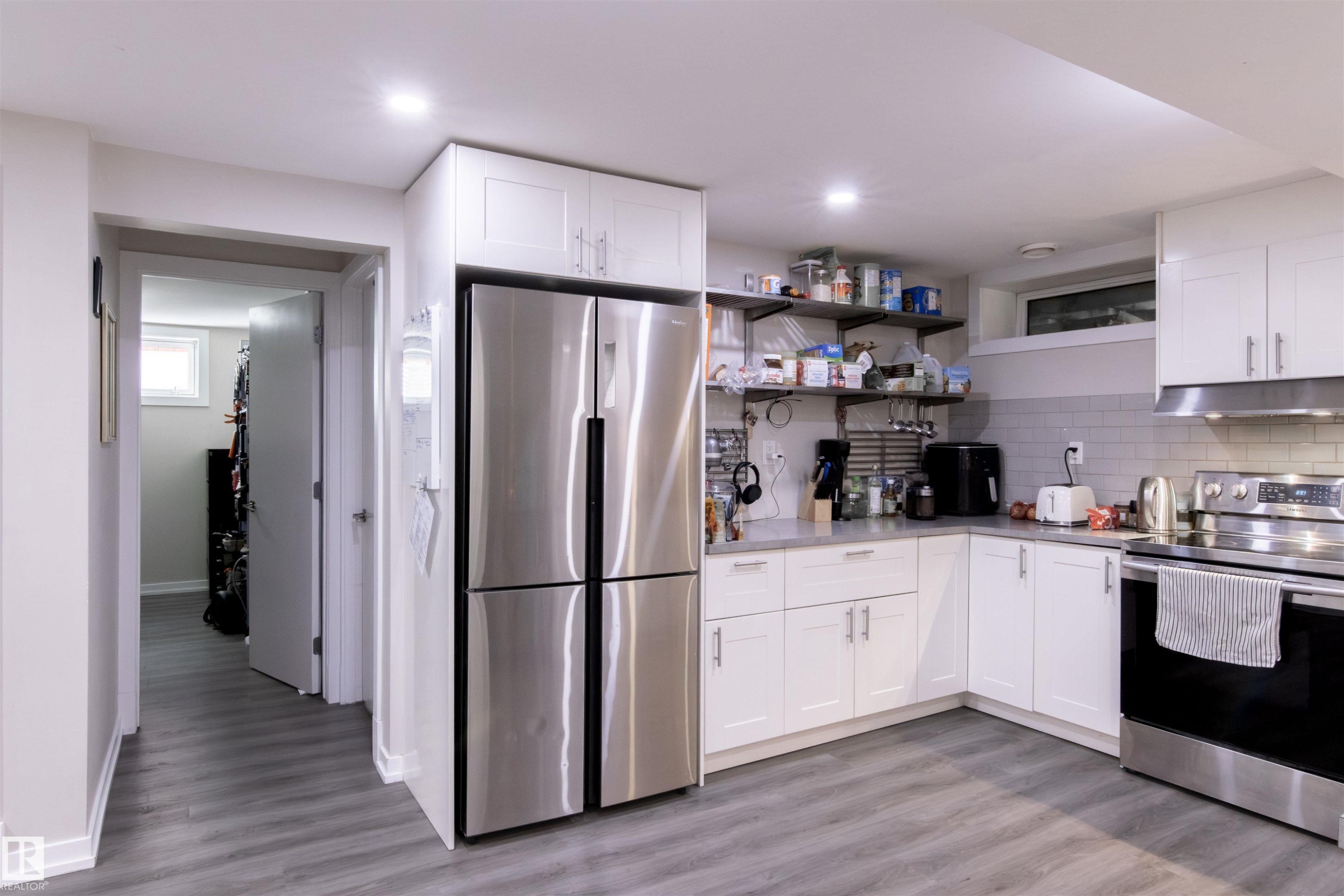 Contemporary kitchen featuring white cabinetry, stainless steel appliances, a subway tile backsplash, and light wood-finish flooring - 7115 39A Avenue, Edmonton, AB - Indoor Photo Showing Kitchen