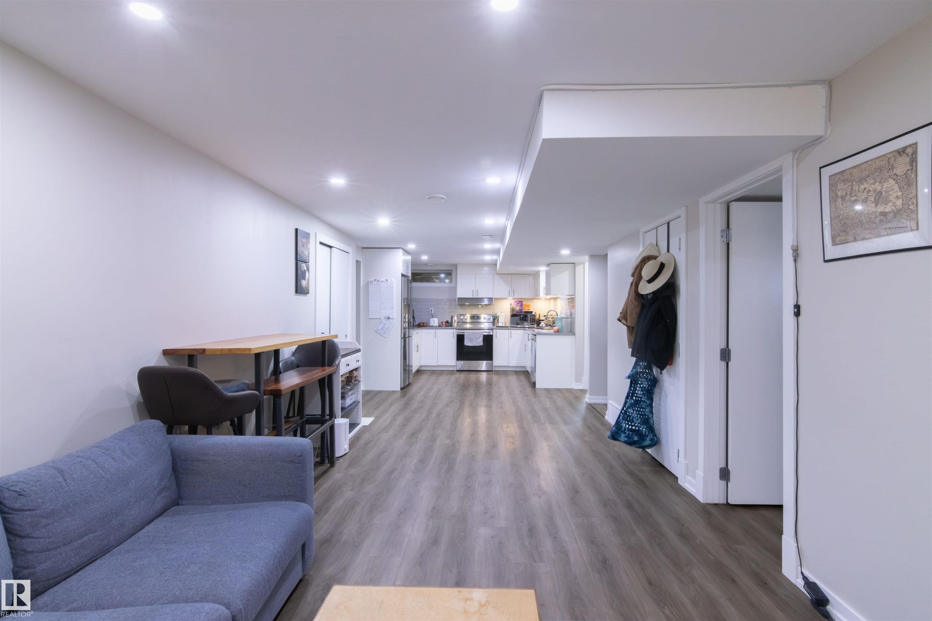 Open-concept living space featuring wood-finish flooring, recessed lighting, and a white kitchen with stainless steel appliances - 7115 39A Avenue, Edmonton, AB - Indoor