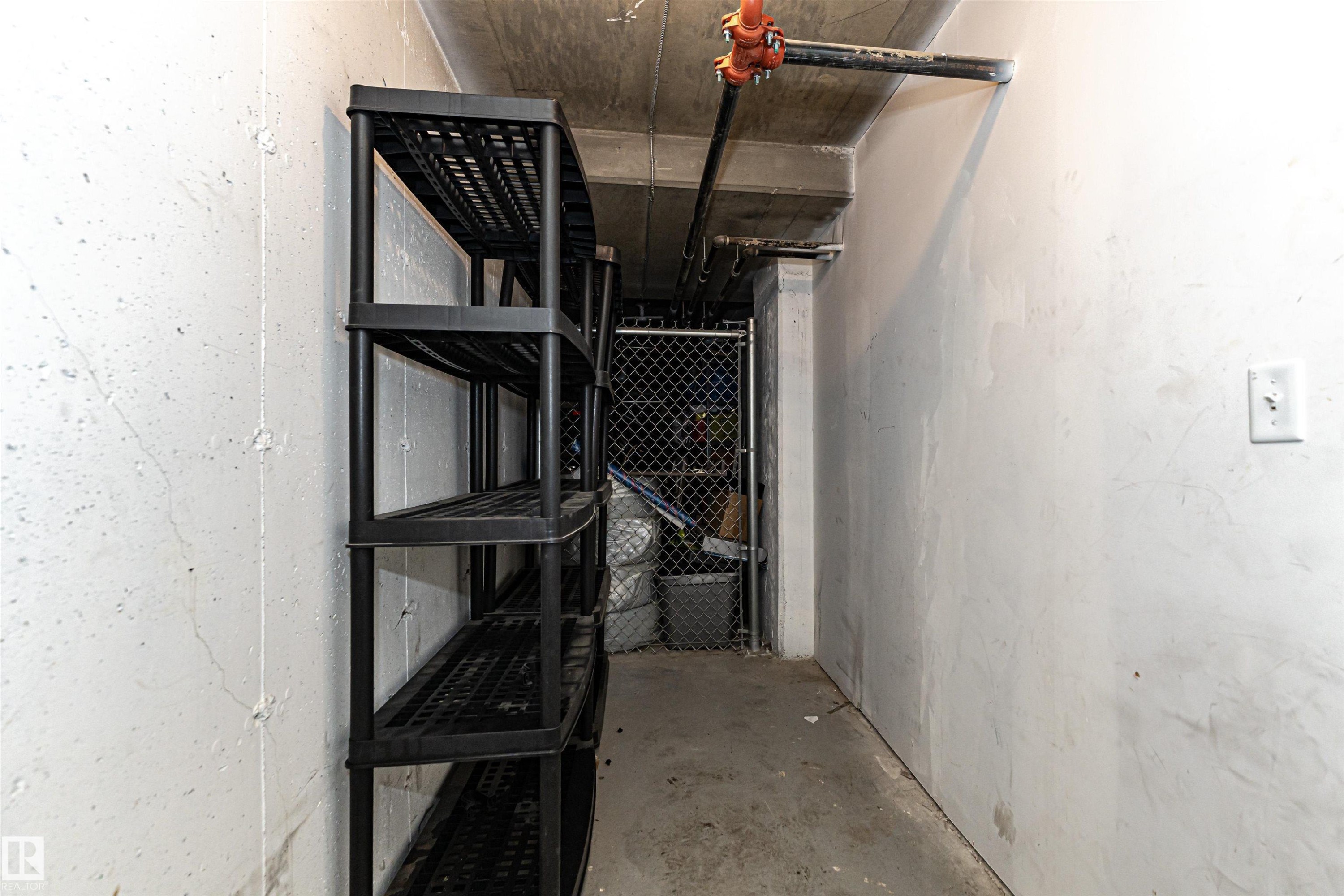 Utility space featuring a stacked shelving unit, concrete flooring, and exposed ceiling utilities - 404 12045 22 Avenue, Edmonton, AB
